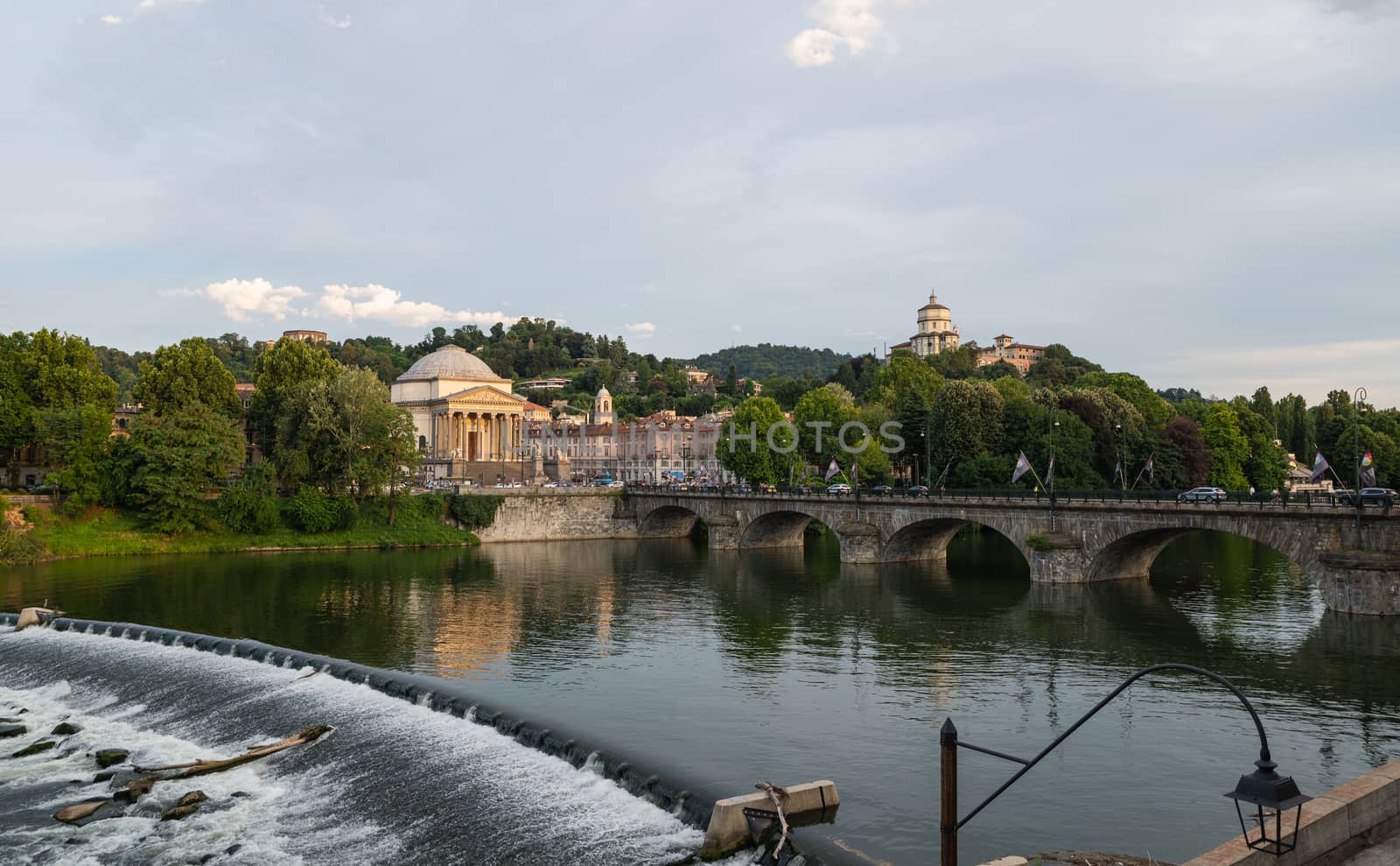 Turin, Piedmont, Italy. July 2020. Wonderful evening view of the Gran Madre church overlooking the Po river. The waterfall downstream of the dam is highlighted. On the bridge people and cars.