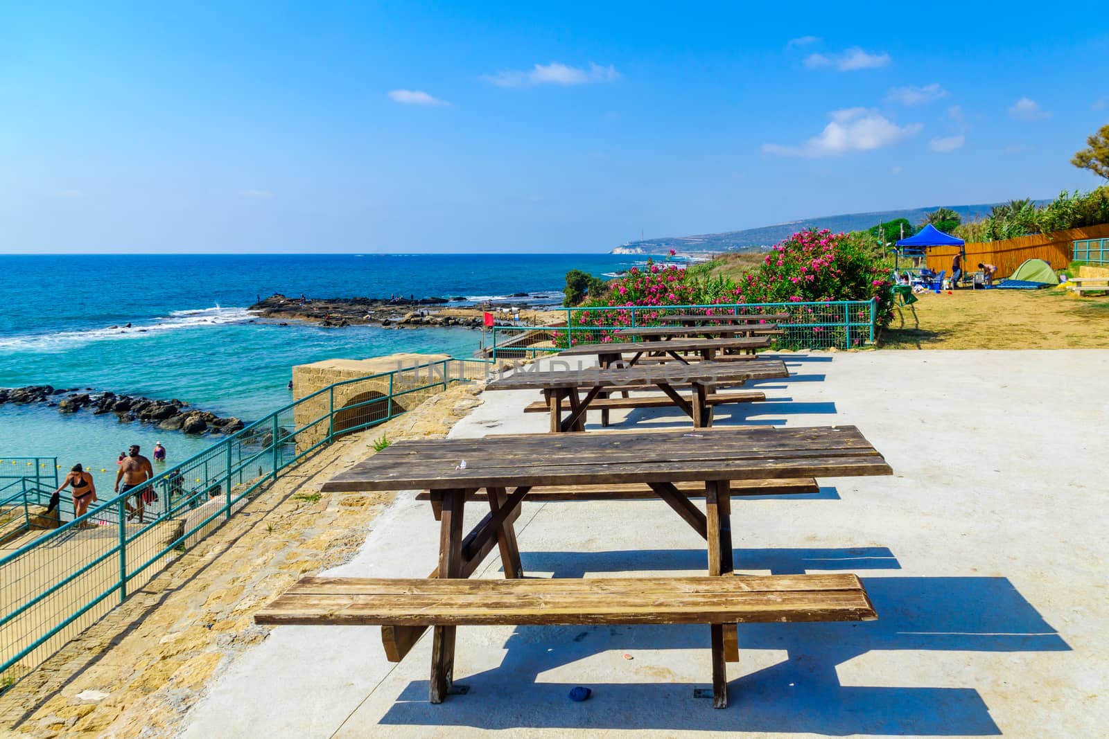 Achziv, Israel - July 22, 2020: View of picnic tables and the coast, with visitors, in Achziv national park, northern Israel