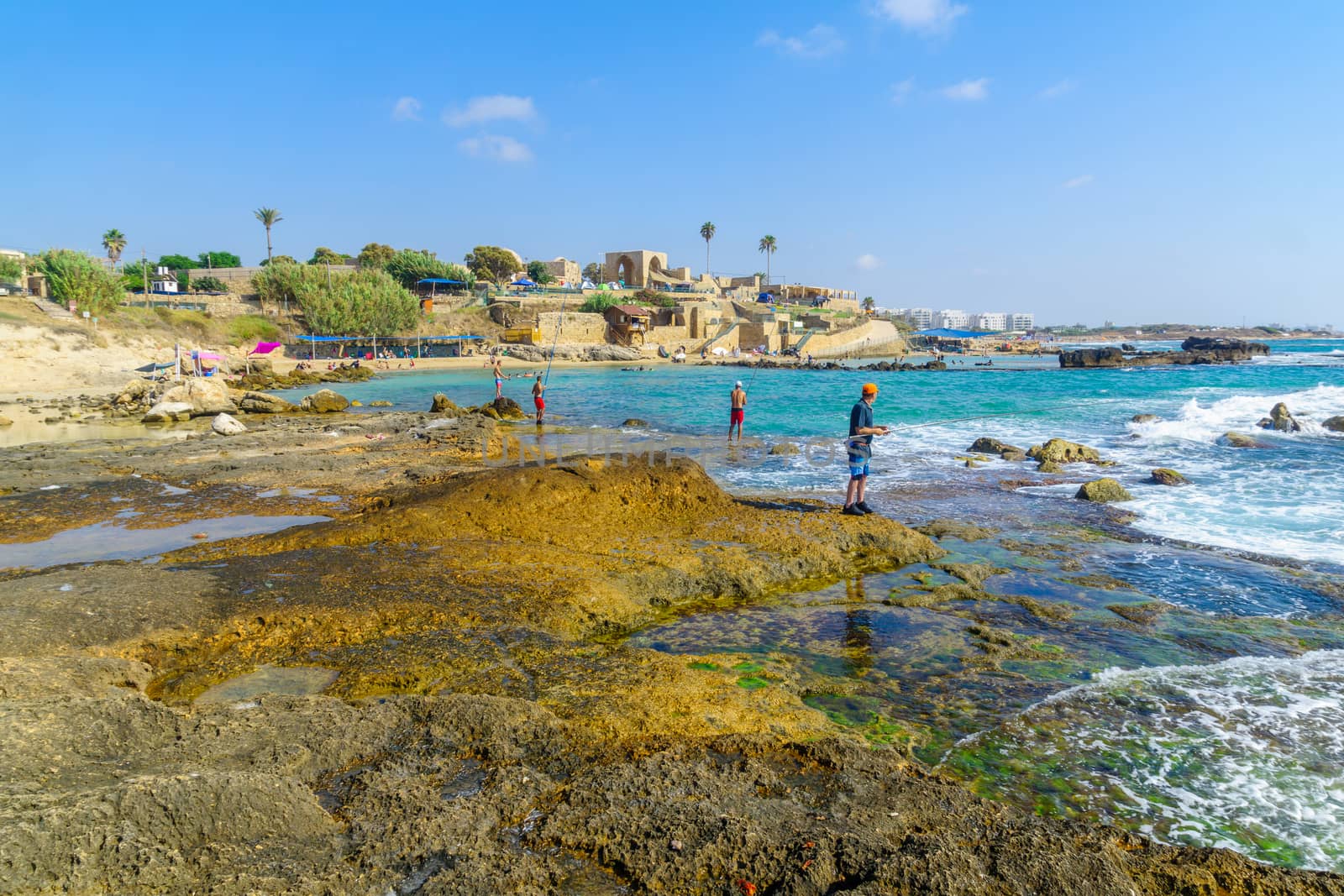 Achziv, Israel - July 22, 2020: View of visitors fishing and bathing, bay, coast, and old buildings, in Achziv national park, northern Israel