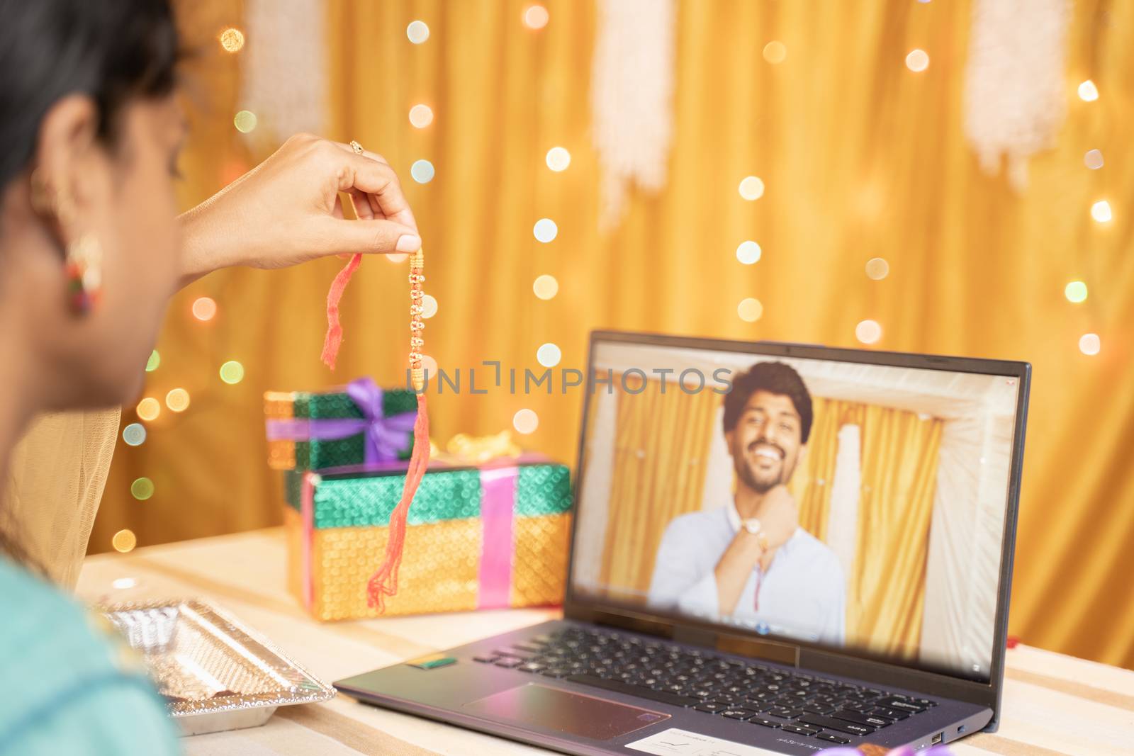 shoulder view of sister video calling her brother to tie rakhi or Raksha Bandhan during festival and showing gift received - Concept of far Rakshabandhan celebration by using technology and internet. by lakshmiprasad.maski@gmai.com