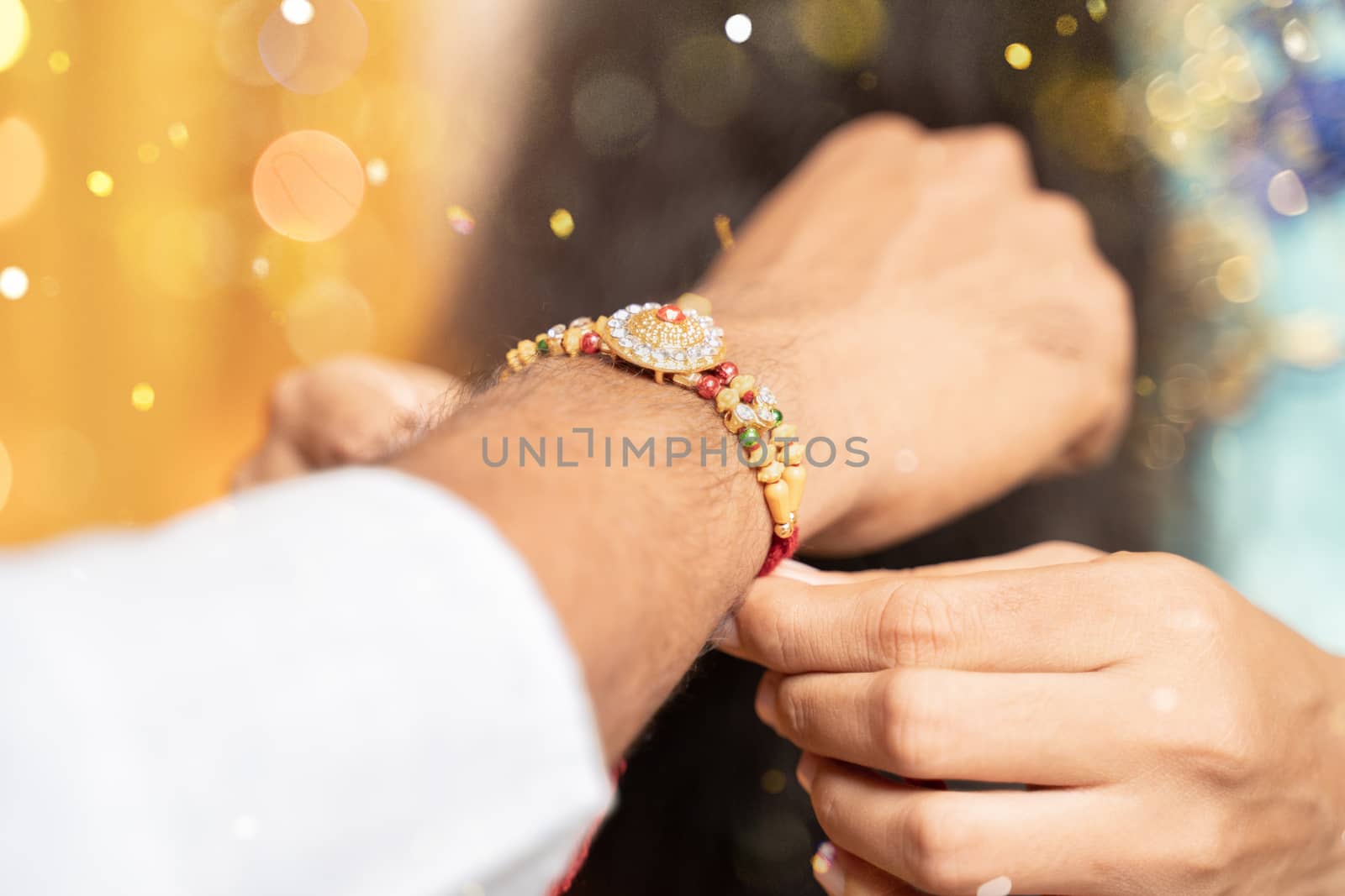 Closeup of hands, sister tying rakhi, Raksha bandhan to brother's wrist during festival or ceremony - Rakshabandhan celebrated across India as selfless love or relationship between brother and sister by lakshmiprasad.maski@gmai.com