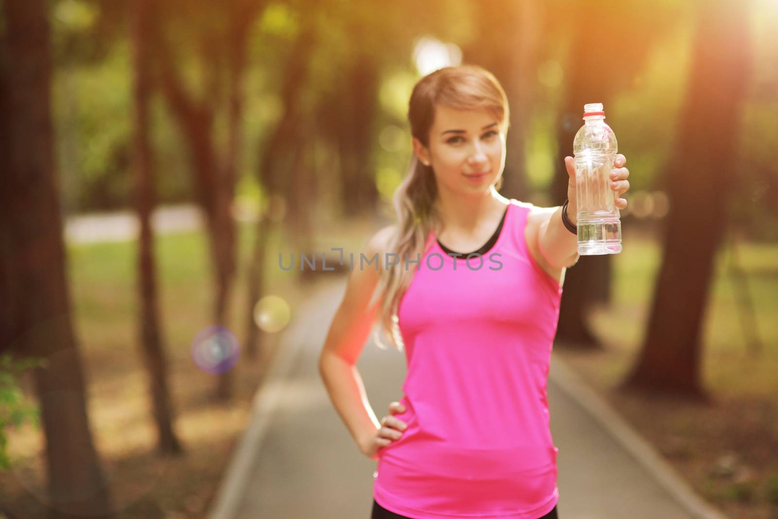 Beautiful fitness athlete runner woman drinking water in the park. Portrait face of a young woman holding a water bottle in summer. Forest