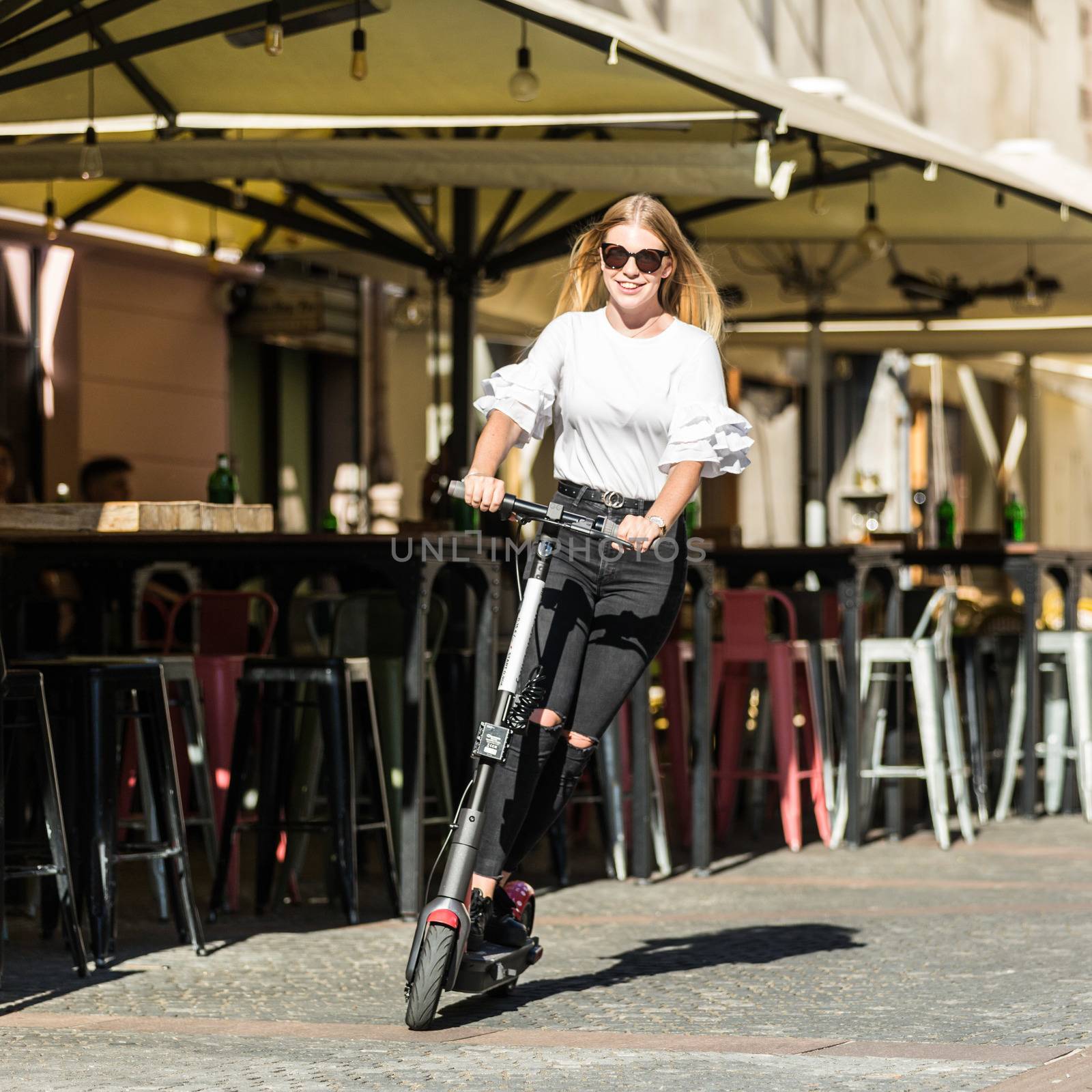 Trendy fashinable teenager girls riding public rental electric scooters in urban city environment. New eco-friendly modern public city transport in Ljubljana, Slovenia by kasto