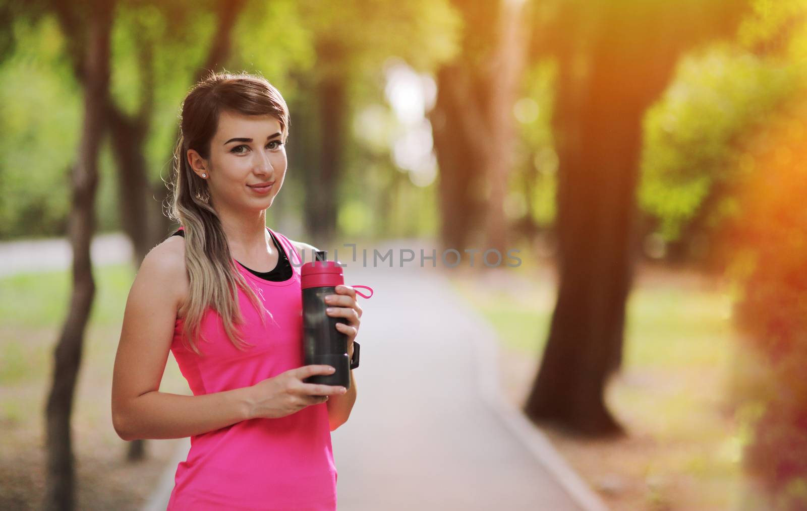 Beautiful fitness athlete runner woman drinking water in the park. Portrait face of a young woman holding a water bottle in summer. Forest