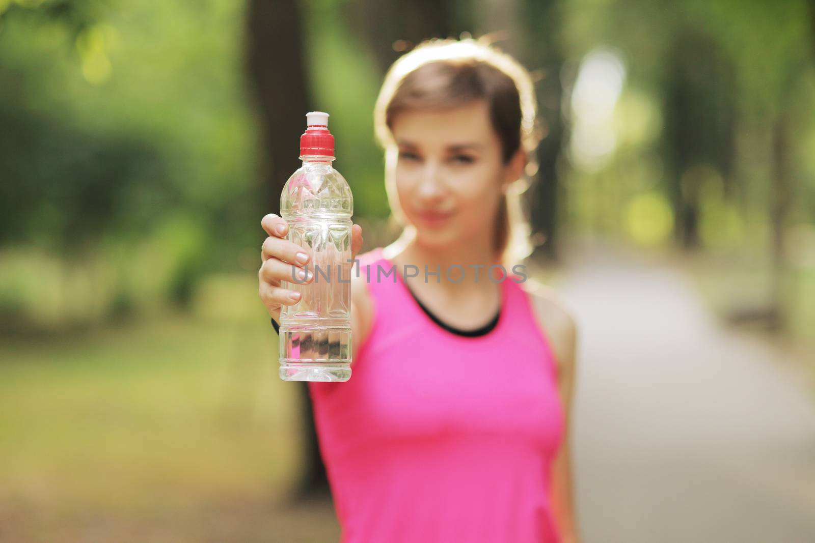 Beautiful fitness athlete runner woman drinking water in the park. Portrait face of a young woman holding a water bottle in summer. Forest