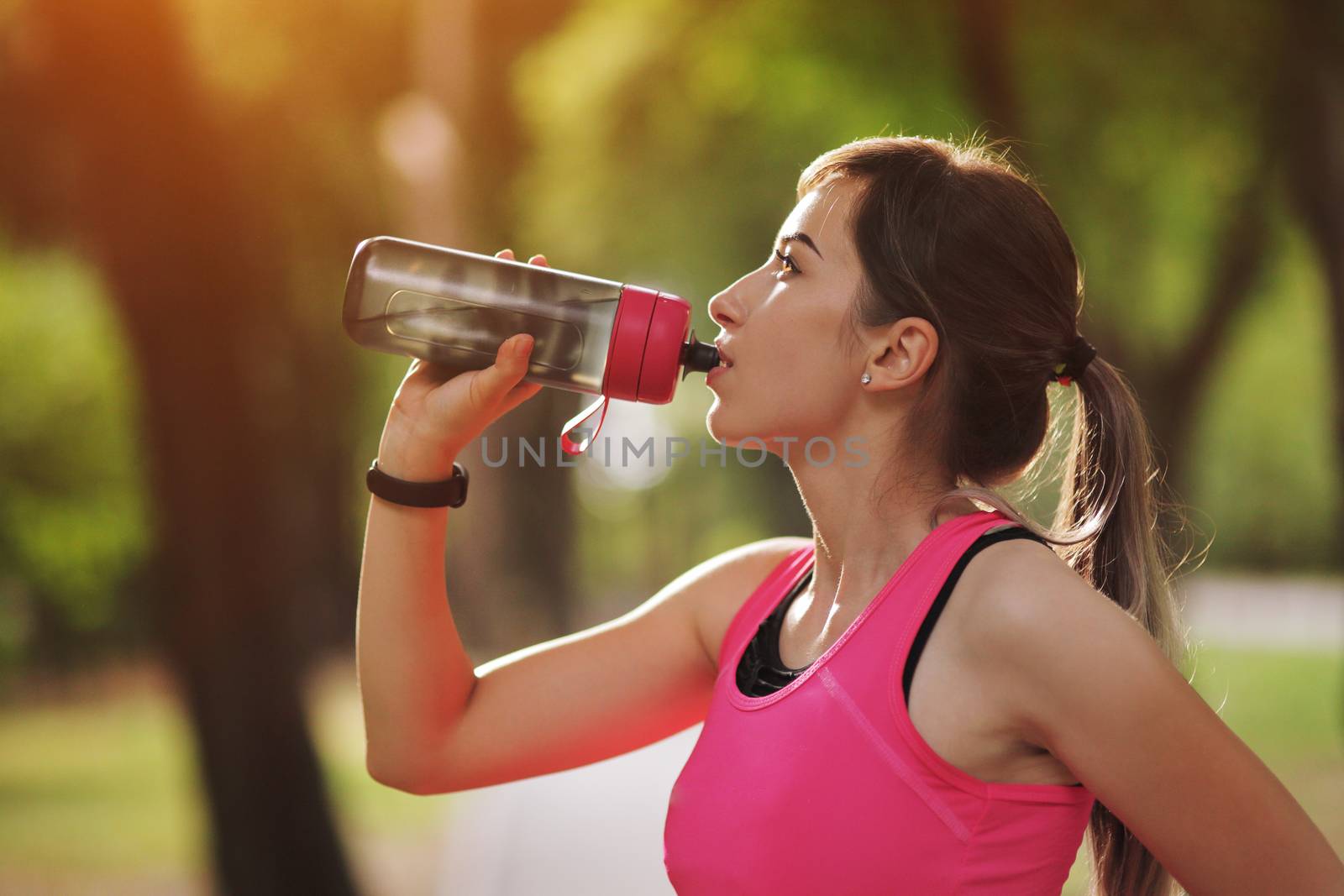 Beautiful fitness athlete runner woman drinking water in the park. Portrait face of a young woman holding a water bottle in summer. Forest