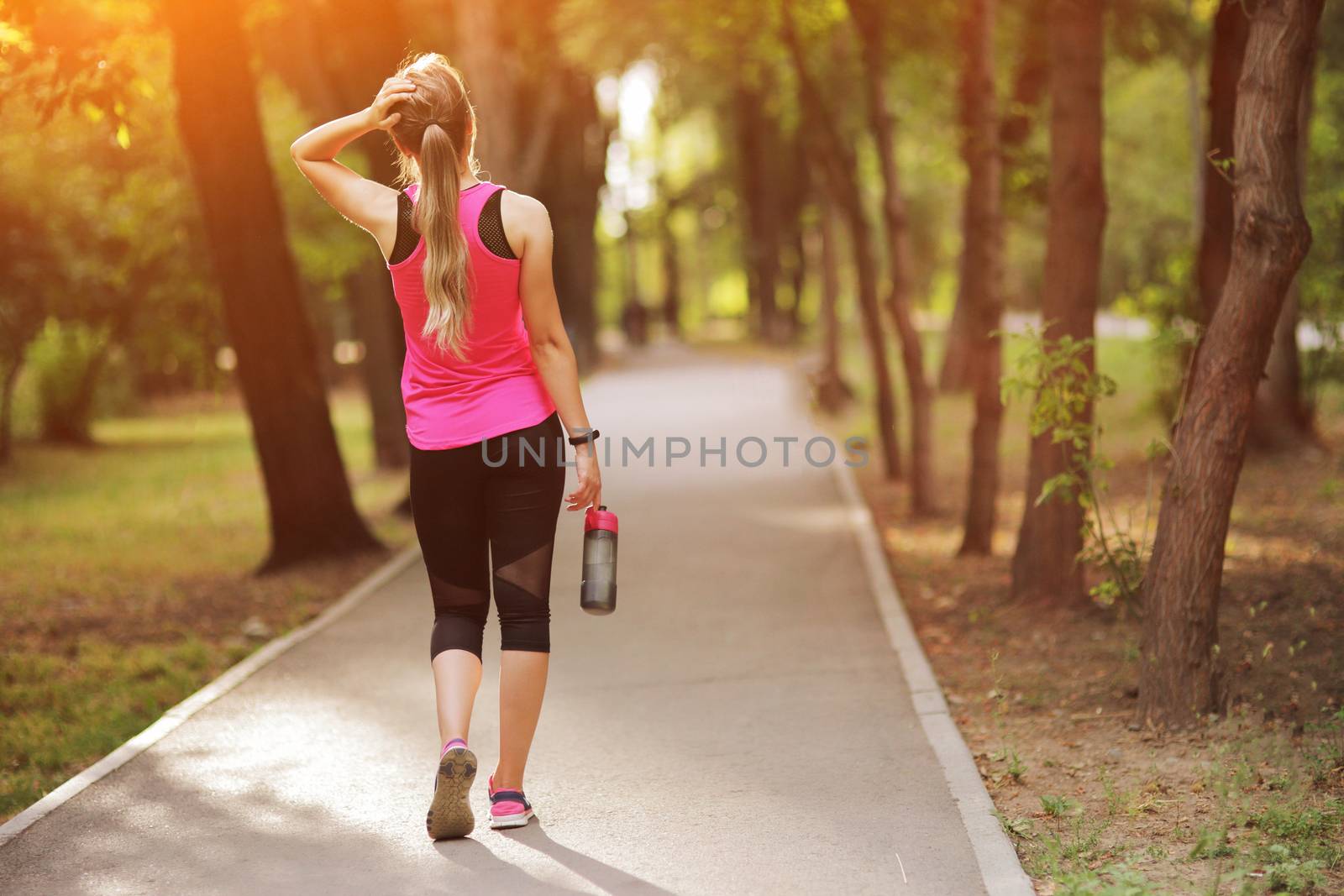 Beautiful fitness athlete runner woman drinking water in the park. Portrait face of a young woman holding a water bottle in summer. Forest