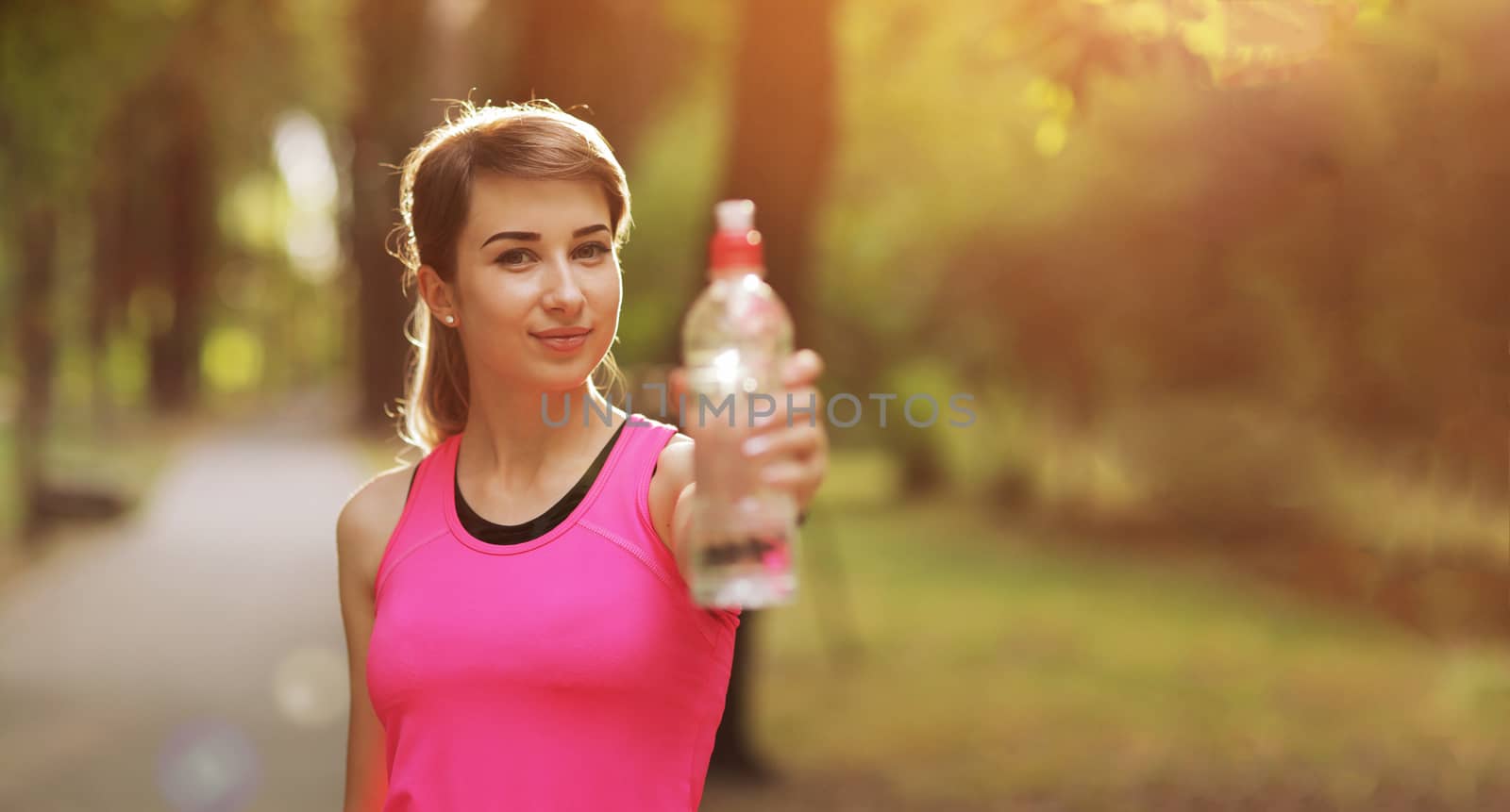 Beautiful fitness athlete runner woman drinking water in the park. Portrait face of a young woman holding a water bottle in summer. Forest