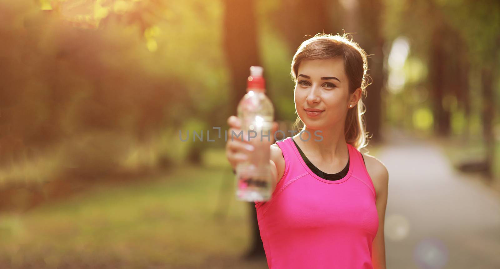 Beautiful fitness athlete runner woman drinking water in the park. Portrait face of a young woman holding a water bottle in summer. Forest