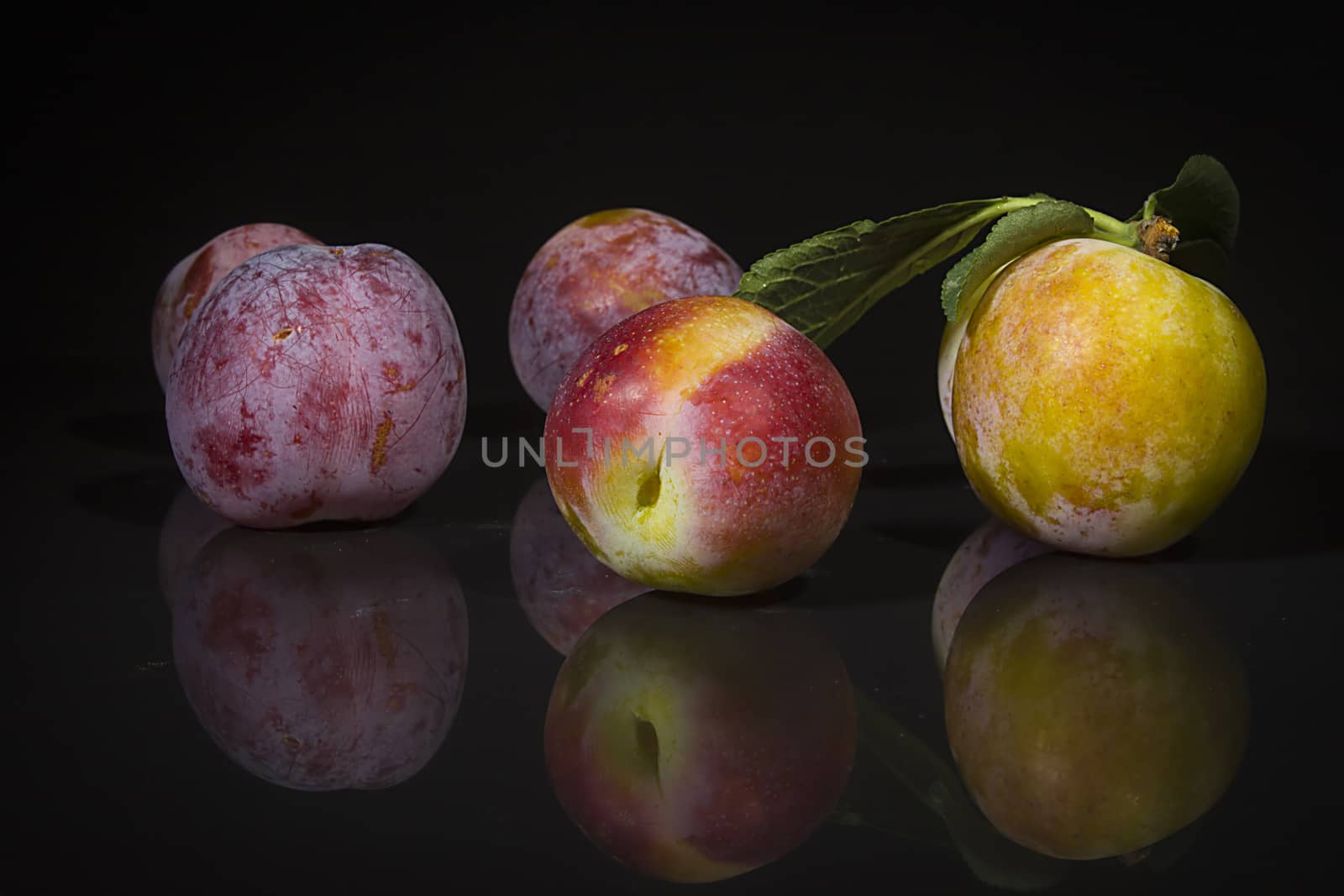 Ripe plums on a black reflective surface