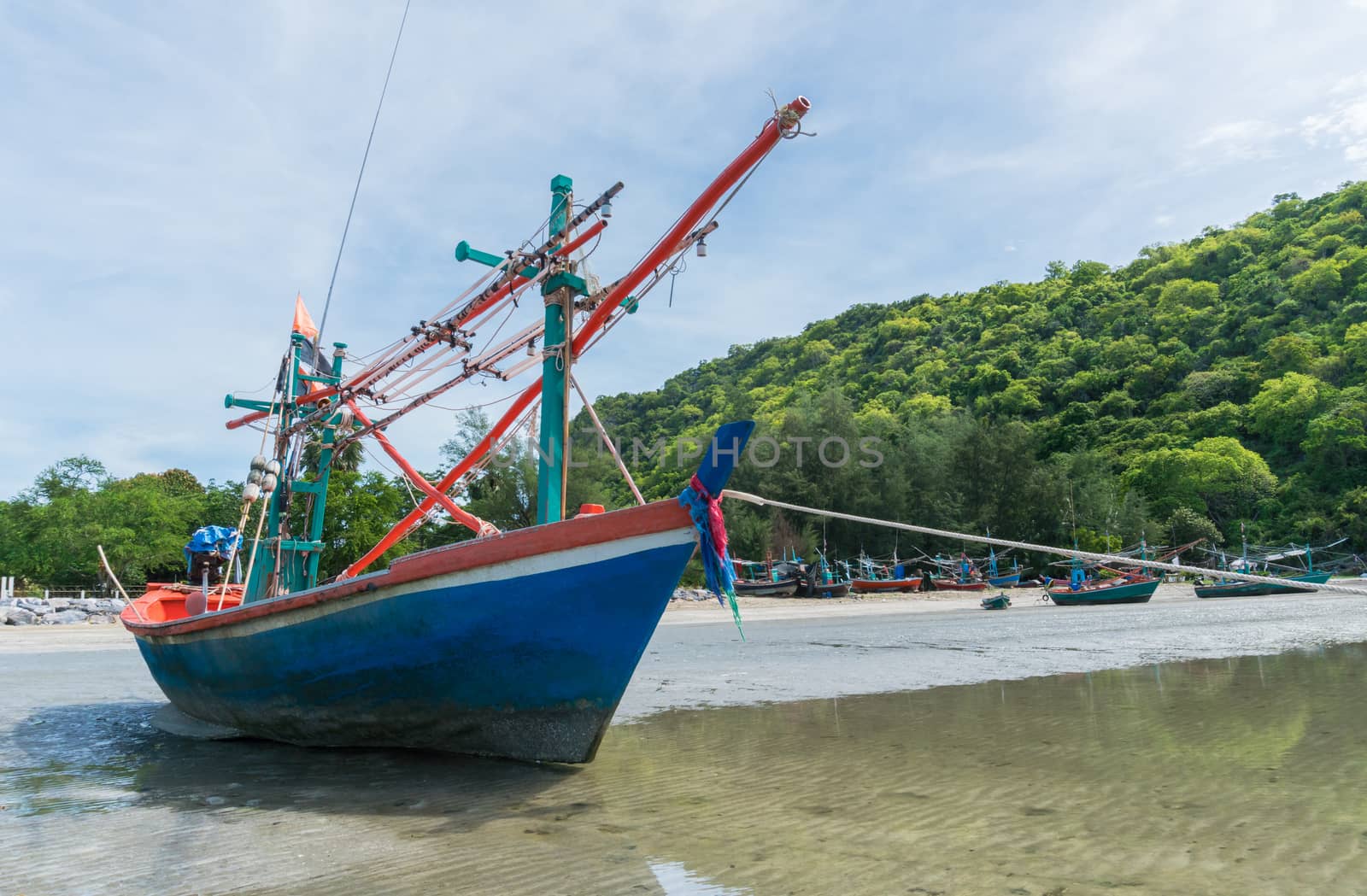 Blue fishing boat on sea sand with green hill and other boat of fisherman at Khao Kalok beach Thailand. Fisherman boat on gray sand with tree 
mountain or tree hill on the beach