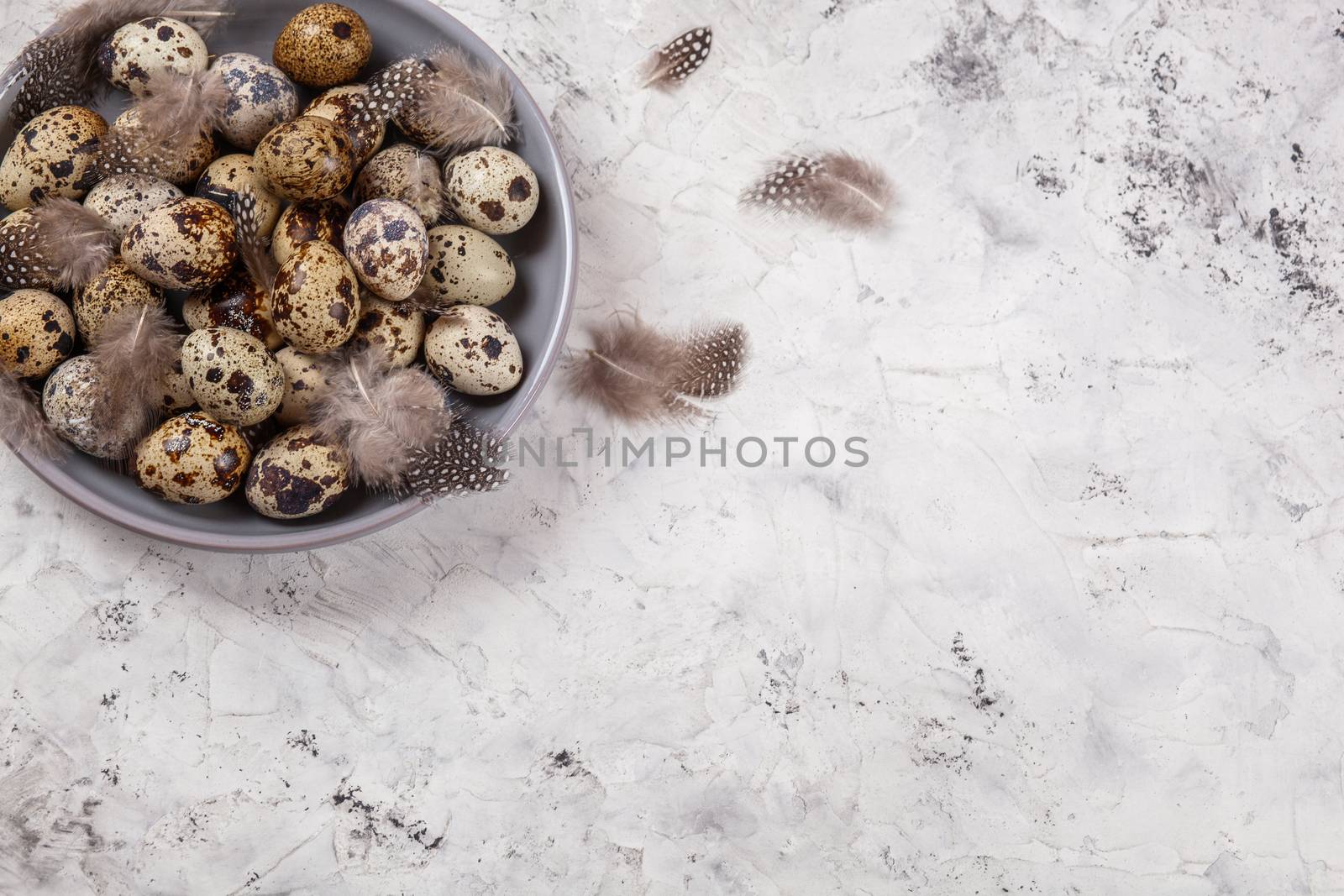 pile of Easter quail eggs on gray fabric cotton rag on concrete background, Round ceramic plate. Space for text
