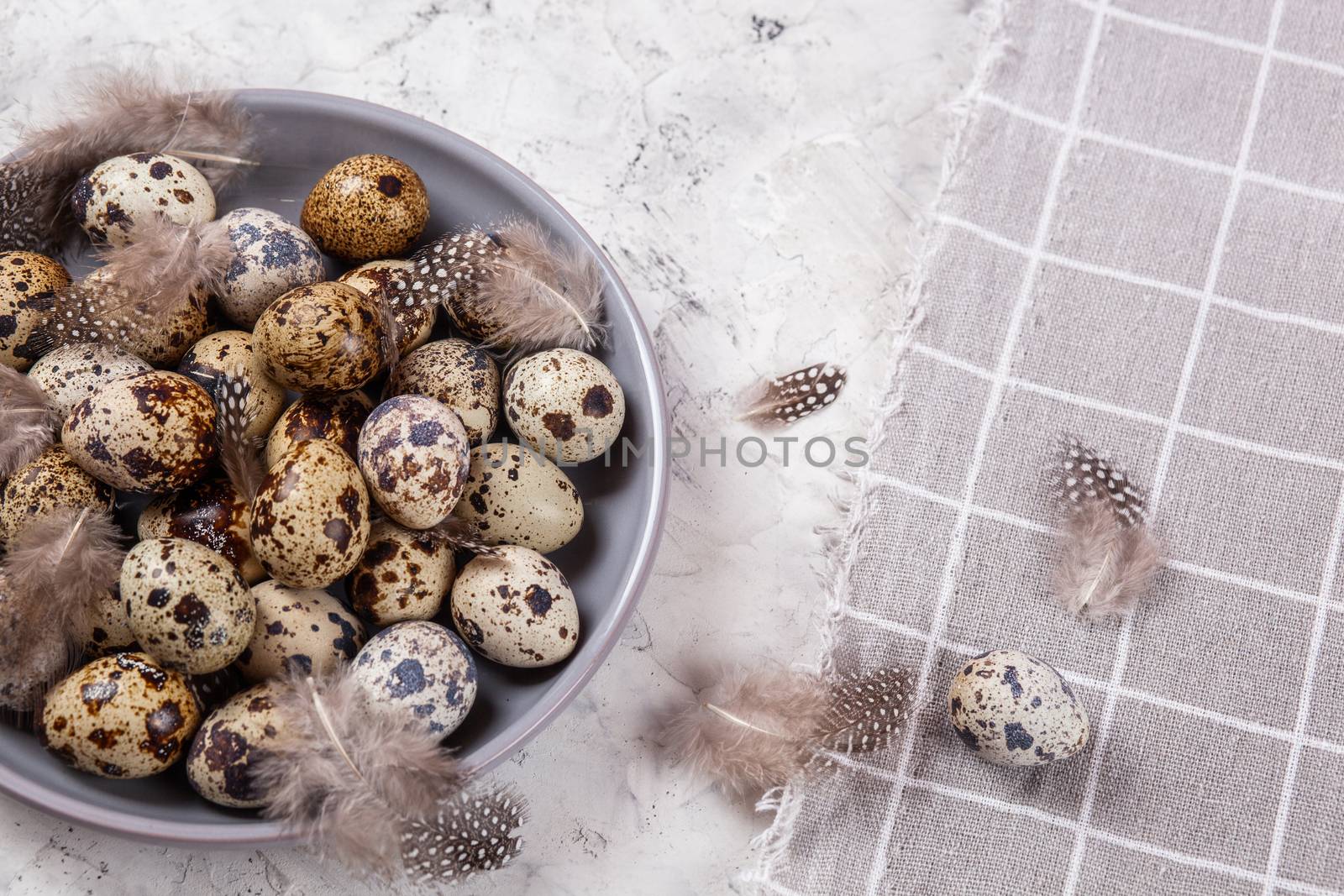 pile of Easter quail eggs on gray fabric cotton rag on concrete background, Round ceramic plate. Space for text