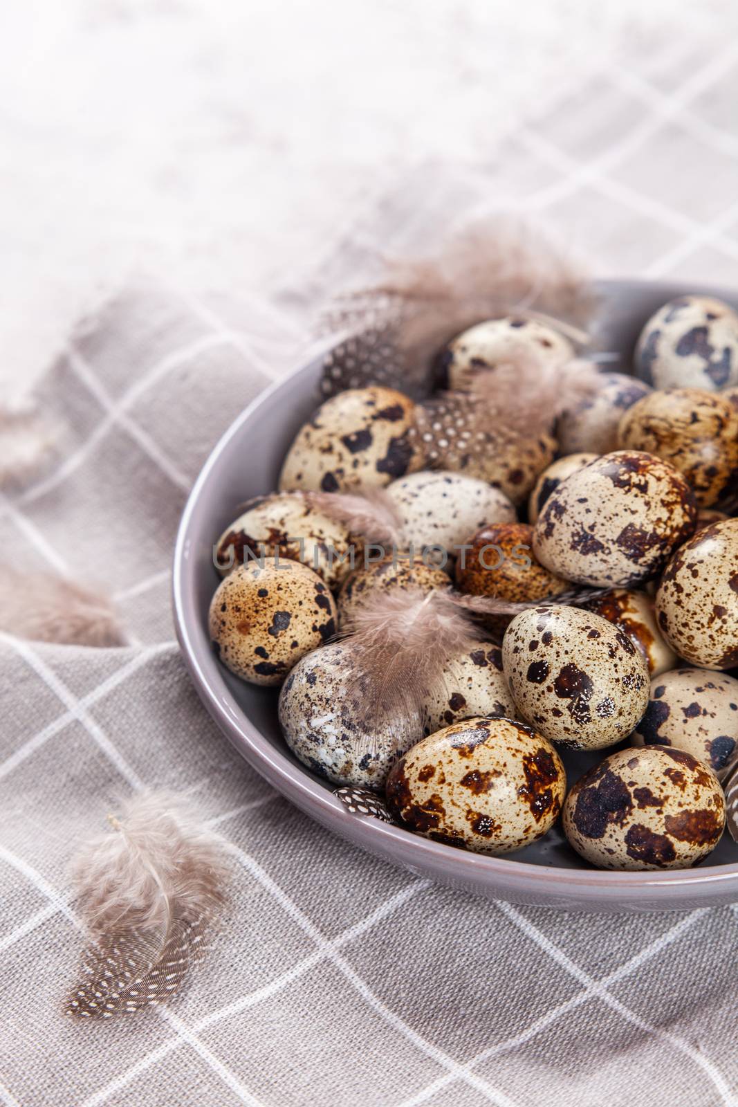 pile of Easter quail eggs on gray fabric cotton rag on concrete background, Round ceramic plate. Space for text