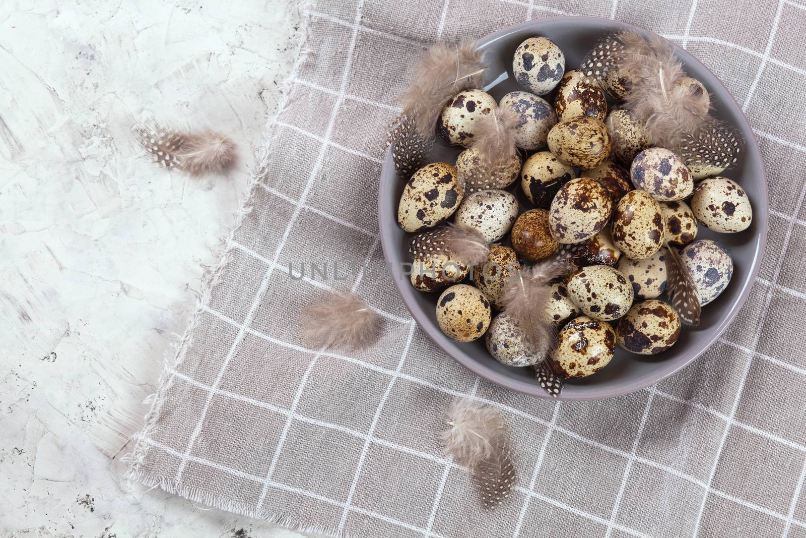 pile of Easter quail eggs on gray fabric cotton rag on concrete background, Round ceramic plate. Space for text