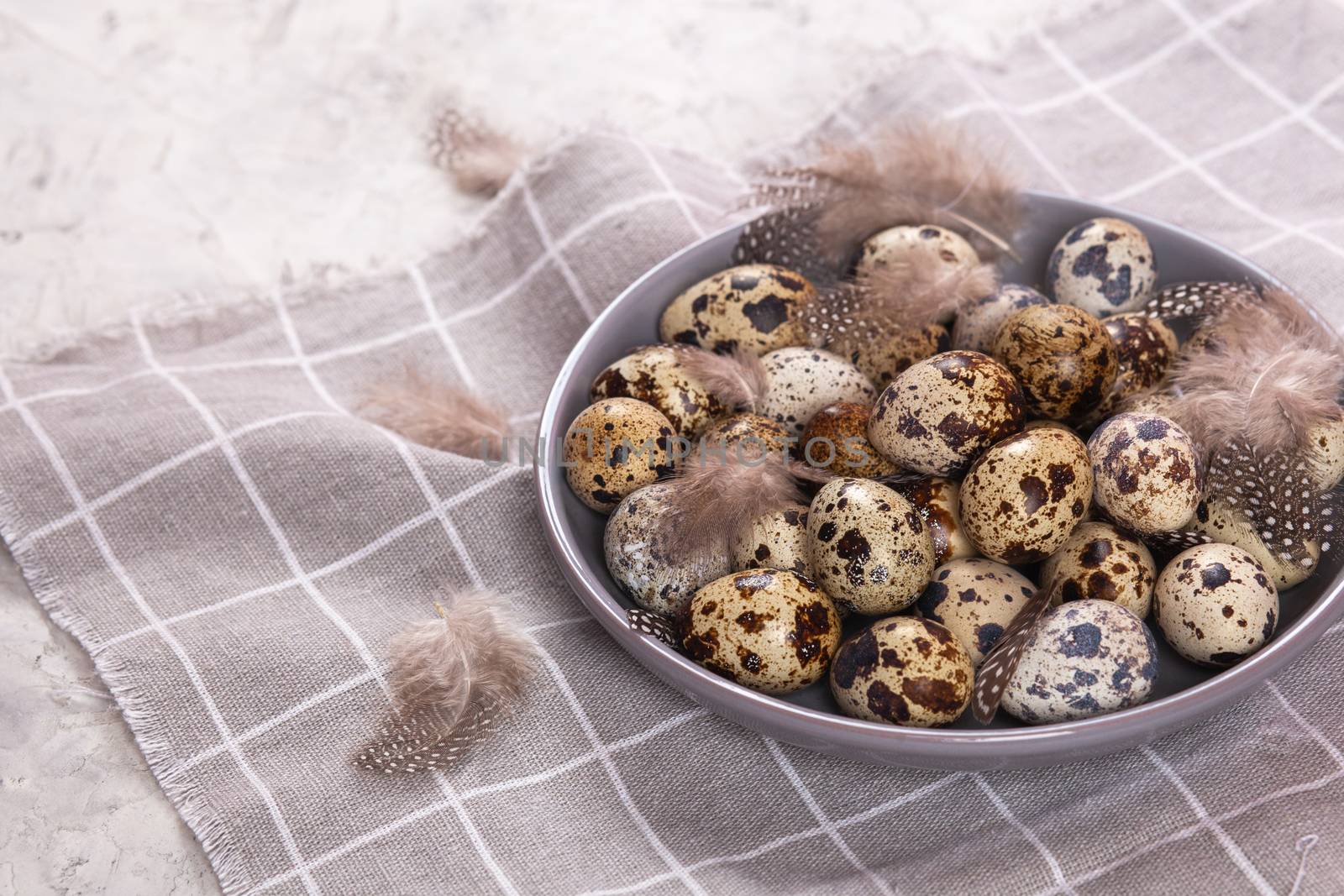 pile of Easter quail eggs on gray fabric cotton rag on concrete background, Round ceramic plate. Space for text
