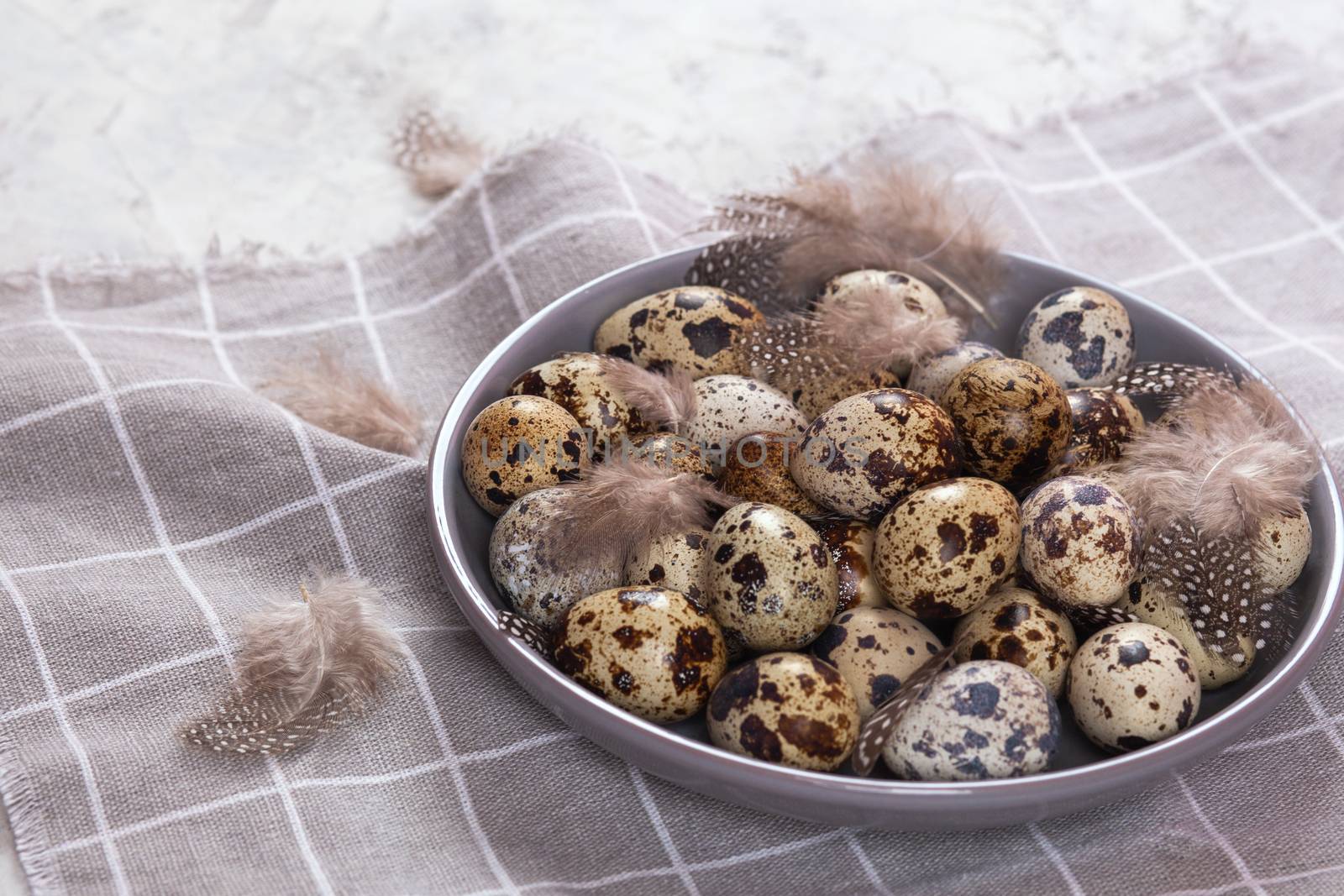 pile of Easter quail eggs on gray fabric cotton rag on concrete background, Round ceramic plate. Space for text