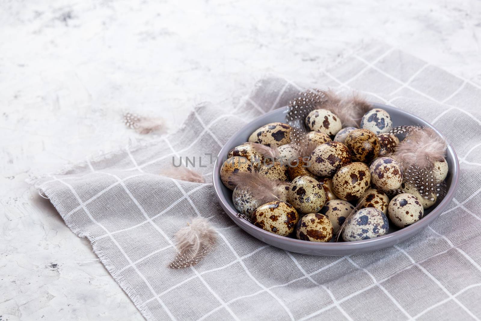 pile of Easter quail eggs on gray fabric cotton rag on concrete background, Round ceramic plate. Space for text