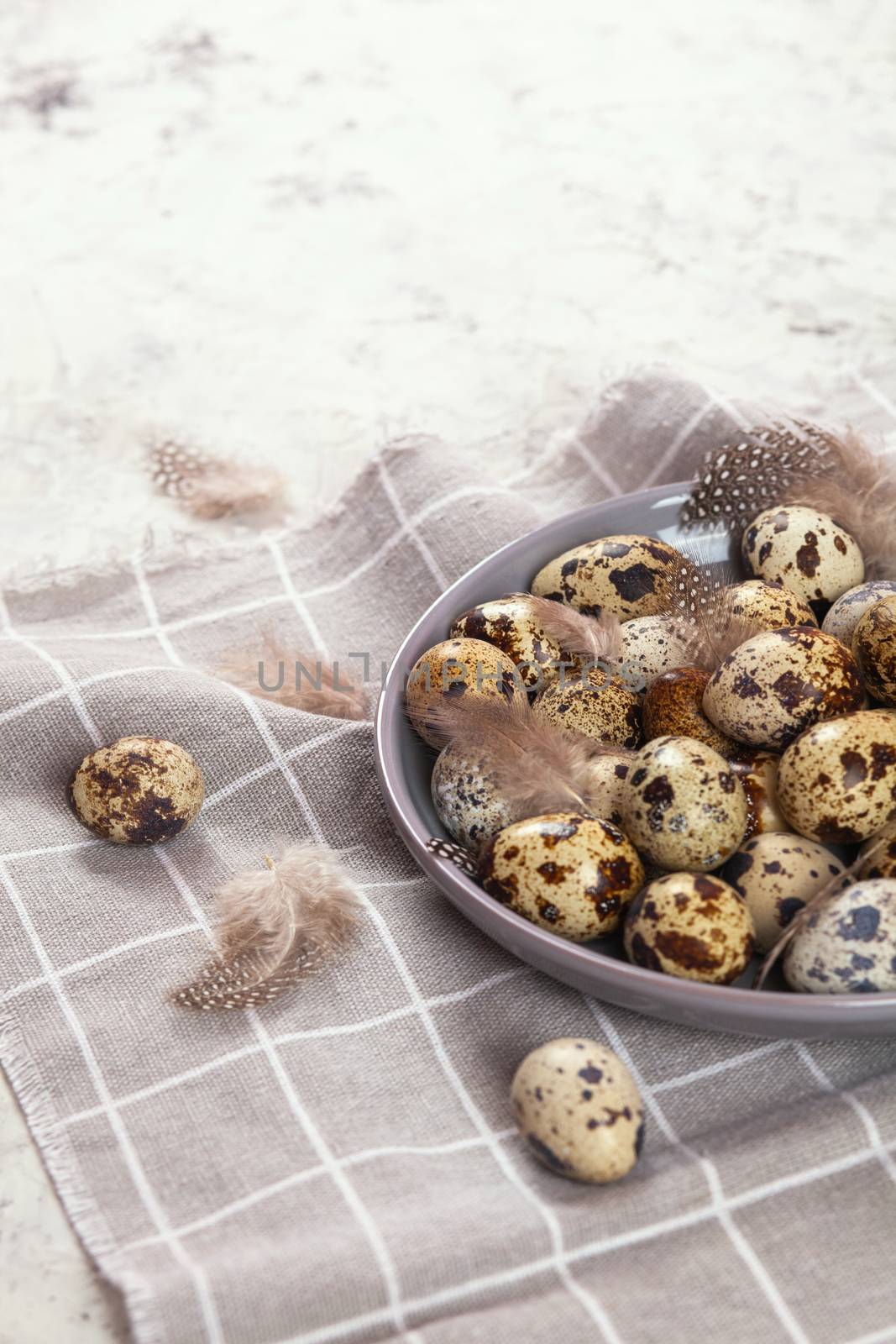 pile of Easter quail eggs on gray fabric cotton rag on concrete background, Round ceramic plate. Space for text