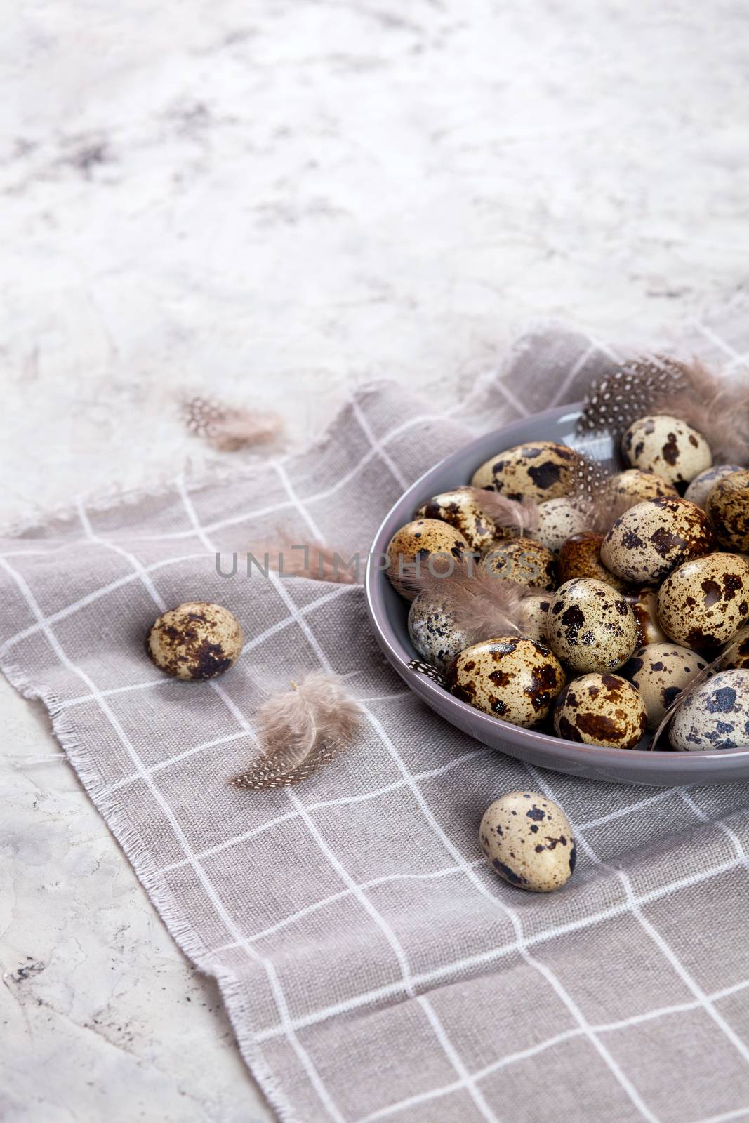 pile of Easter quail eggs on gray fabric cotton rag on concrete background, Round ceramic plate. Space for text