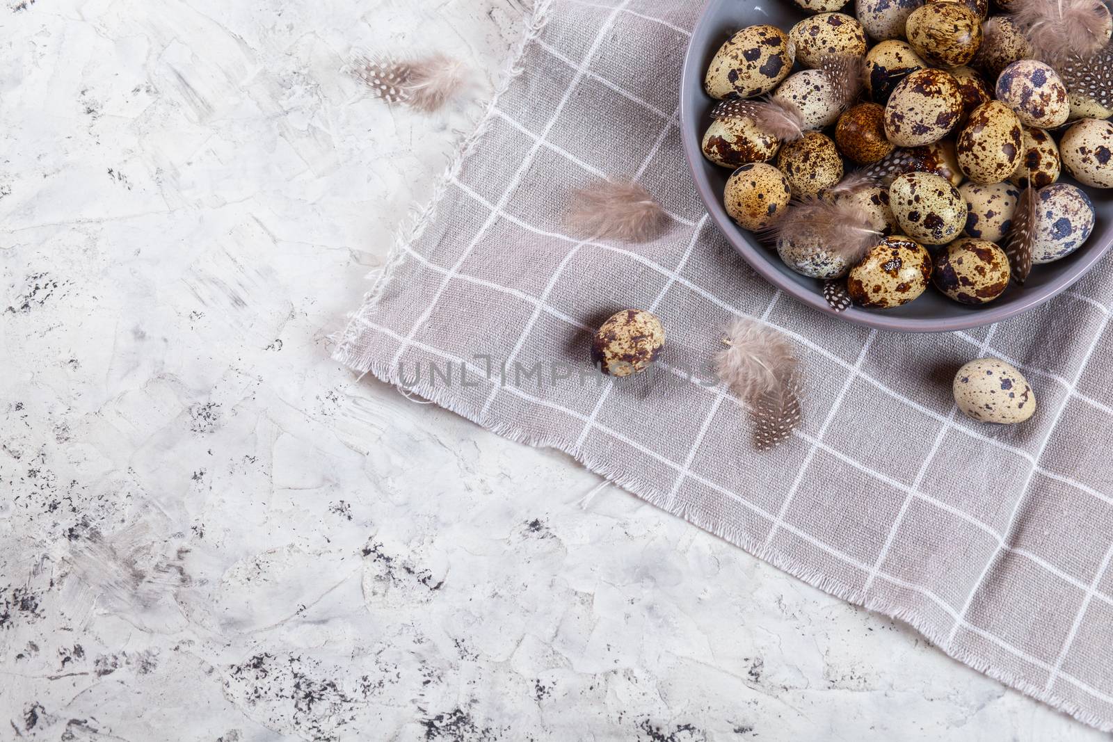pile of Easter quail eggs on gray fabric cotton rag on concrete background, Round ceramic plate. Space for text