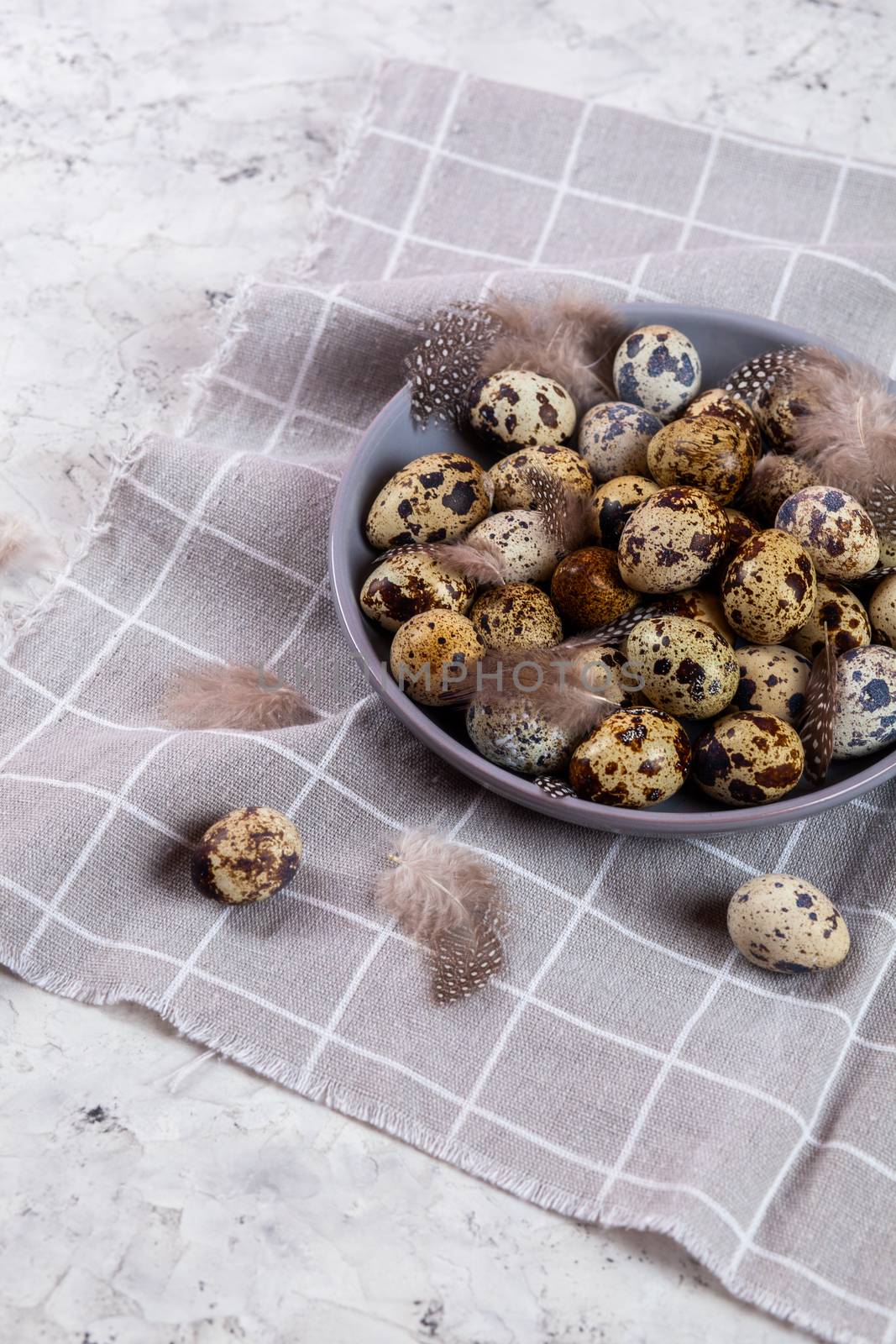 pile of Easter quail eggs on gray fabric cotton rag on concrete background, Round ceramic plate. Space for text