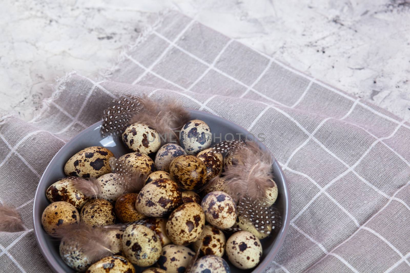 pile of Easter quail eggs on gray fabric cotton rag on concrete background, Round ceramic plate. Space for text