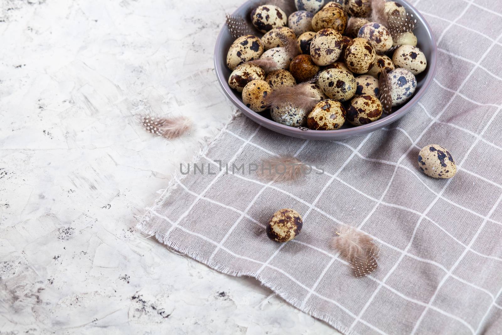 pile of Easter quail eggs on gray fabric cotton rag on concrete background, Round ceramic plate. Space for text