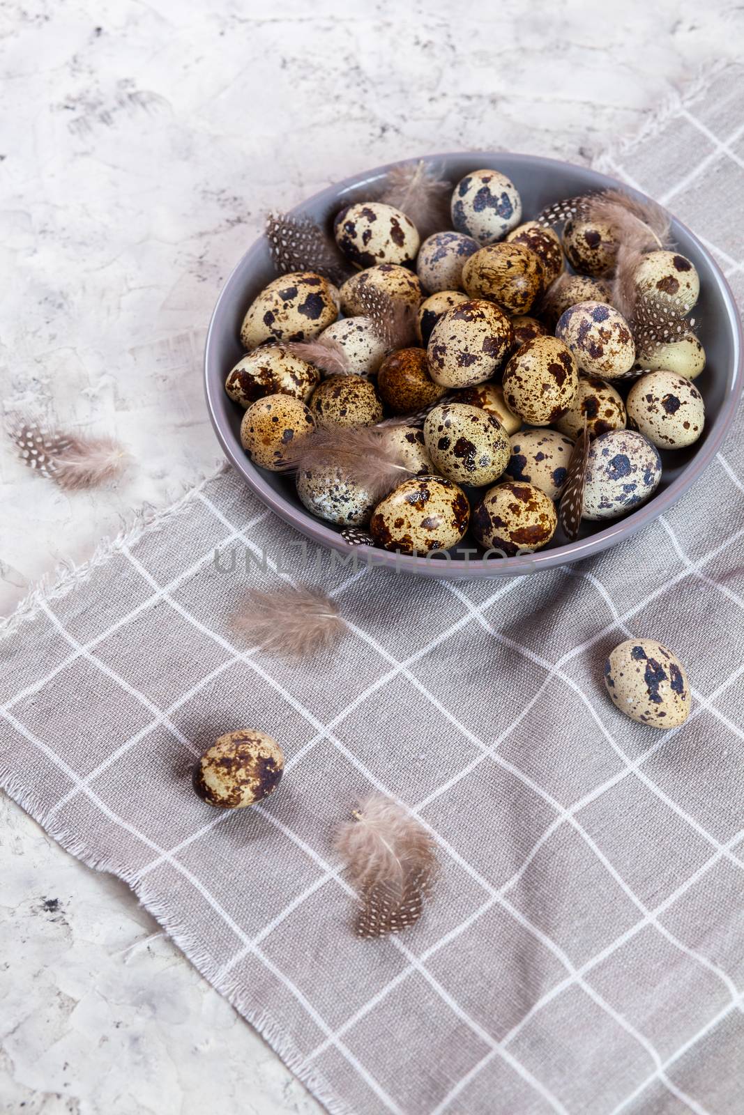 pile of Easter quail eggs on gray fabric cotton rag on concrete background, Round ceramic plate. Space for text