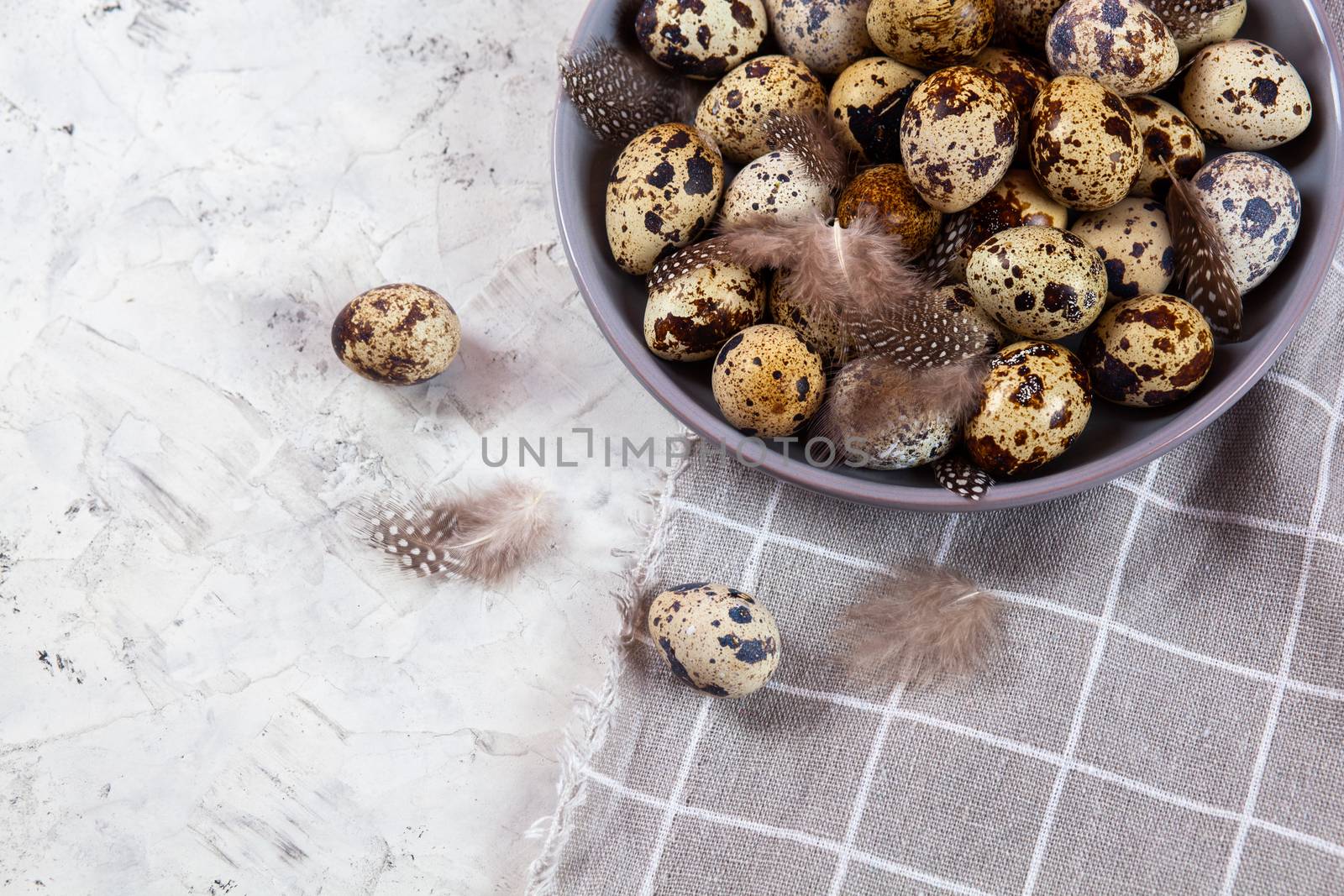 pile of Easter quail eggs on gray fabric cotton rag on concrete background, Round ceramic plate. Space for text
