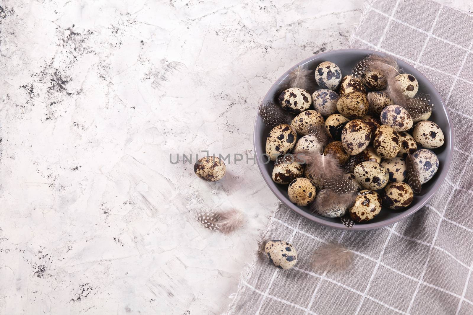 pile of Easter quail eggs on gray fabric cotton rag on concrete background, Round ceramic plate. Space for text