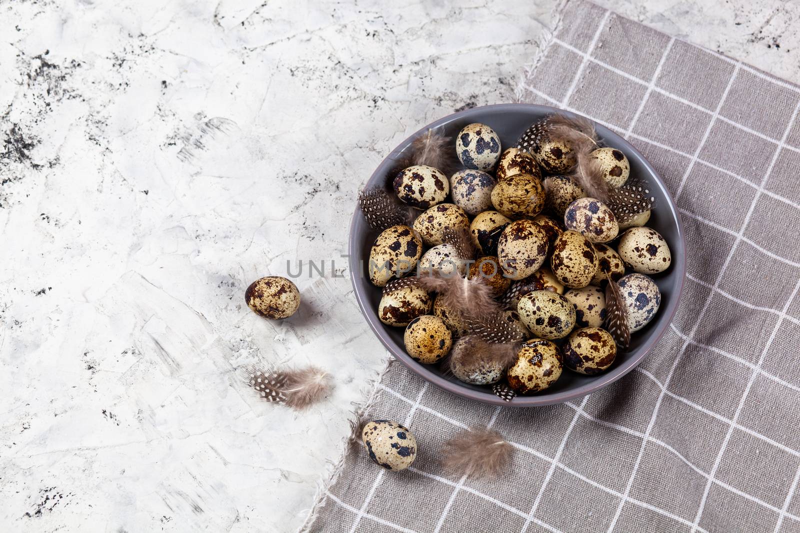 pile of Easter quail eggs on gray fabric cotton rag on concrete background, Round ceramic plate. Space for text