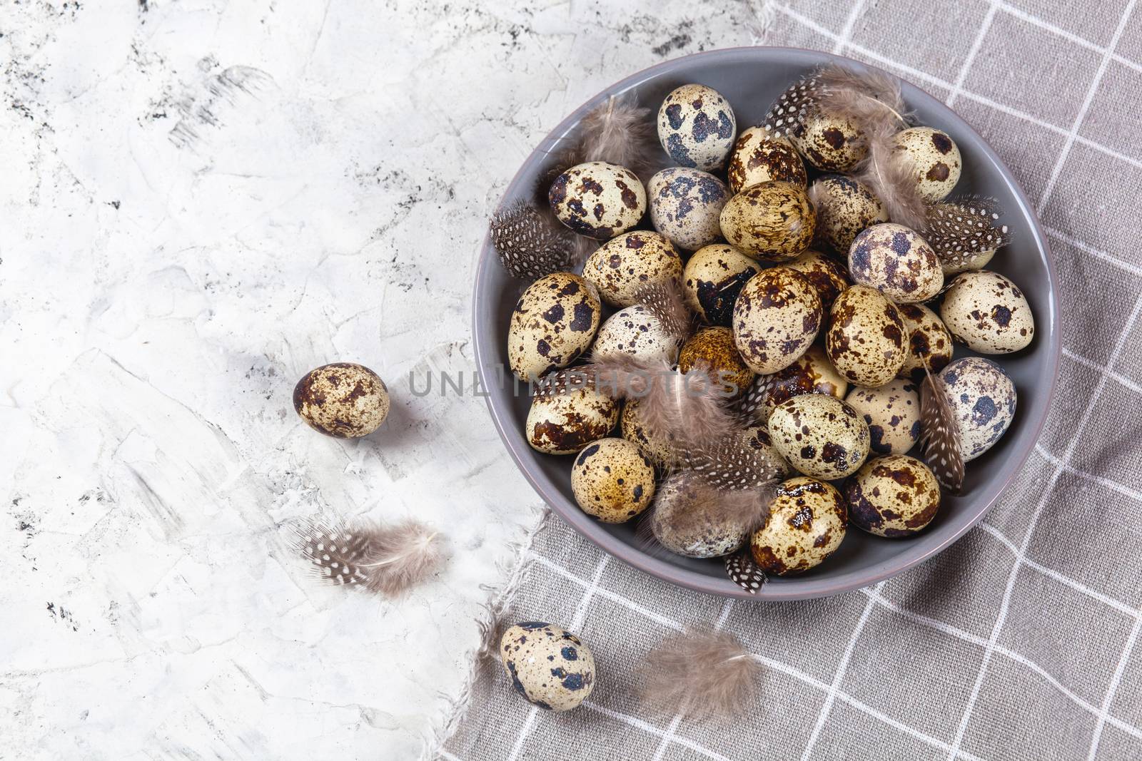 pile of Easter quail eggs on gray fabric cotton rag on concrete background, Round ceramic plate. Space for text