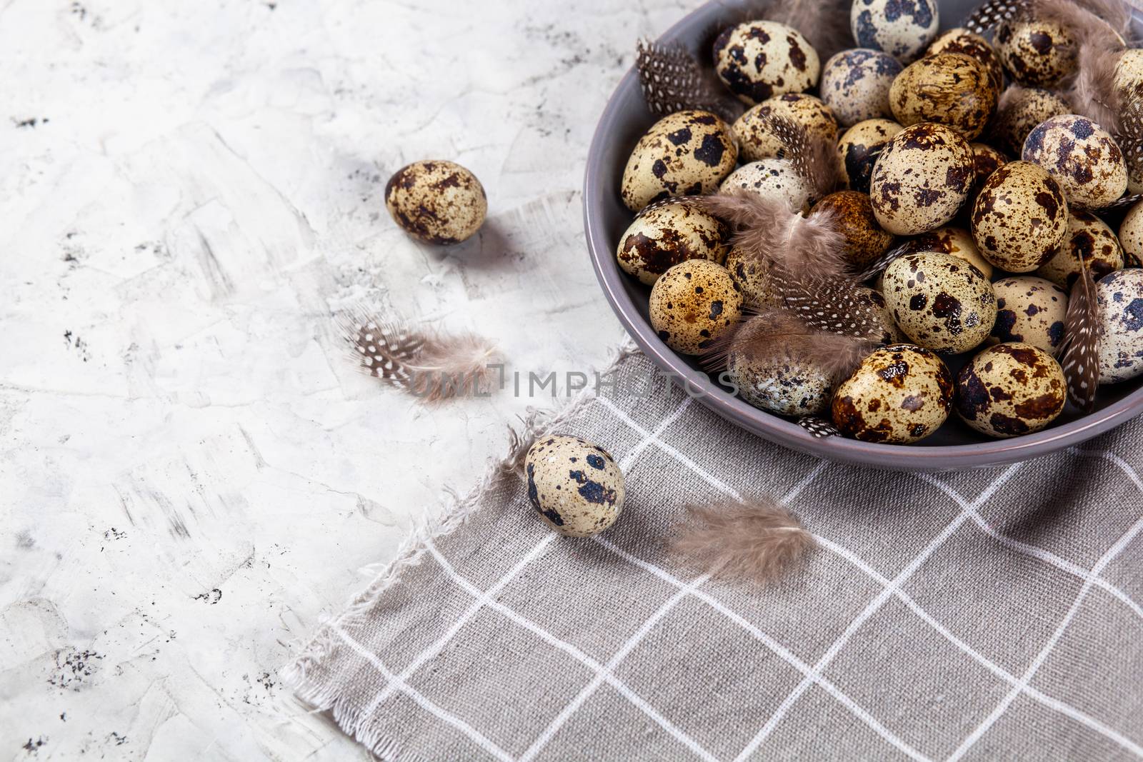 pile of Easter quail eggs on gray fabric cotton rag on concrete background, Round ceramic plate. Space for text