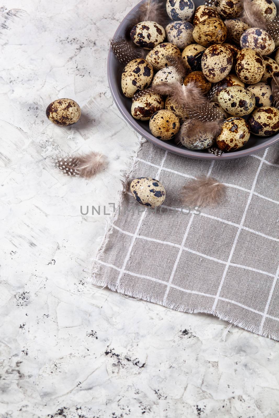 pile of Easter quail eggs on gray fabric cotton rag on concrete background, Round ceramic plate. Space for text