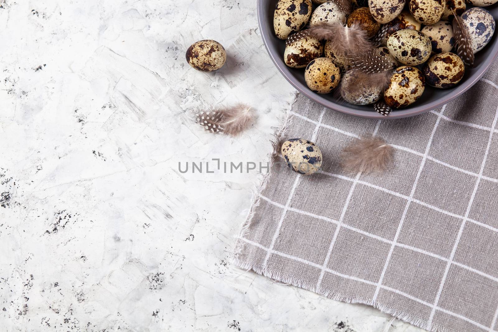 pile of Easter quail eggs on gray fabric cotton rag on concrete background, Round ceramic plate. Space for text