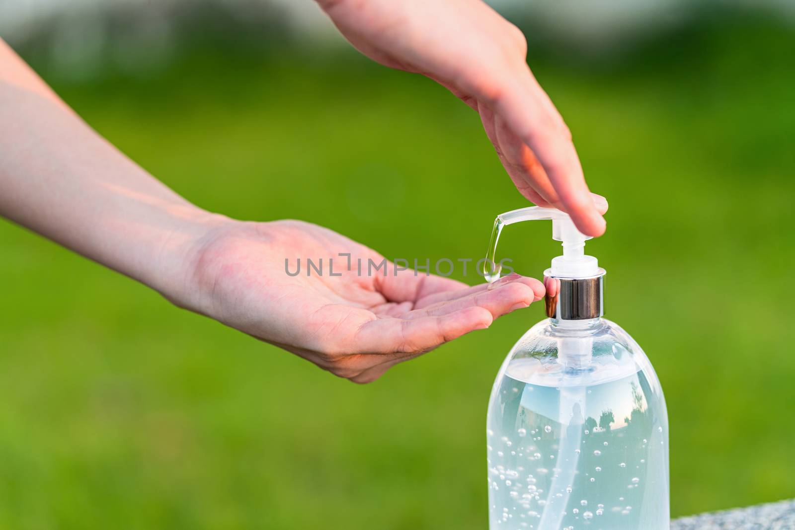 Closeup Asian woman hand using wash hand sanitizer gel pump dispenser before work over photo blurred of green color of grass while Coronavirus Network Outbreak, health care and covid19 concept