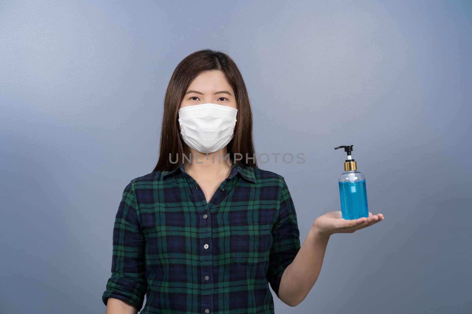 Portrait of asian female wearing face surgical mask and presenting alcohol gel or hand sanitizer on blue color background, covid19 outbreak and pandemic,healthcare and protection against virus concept