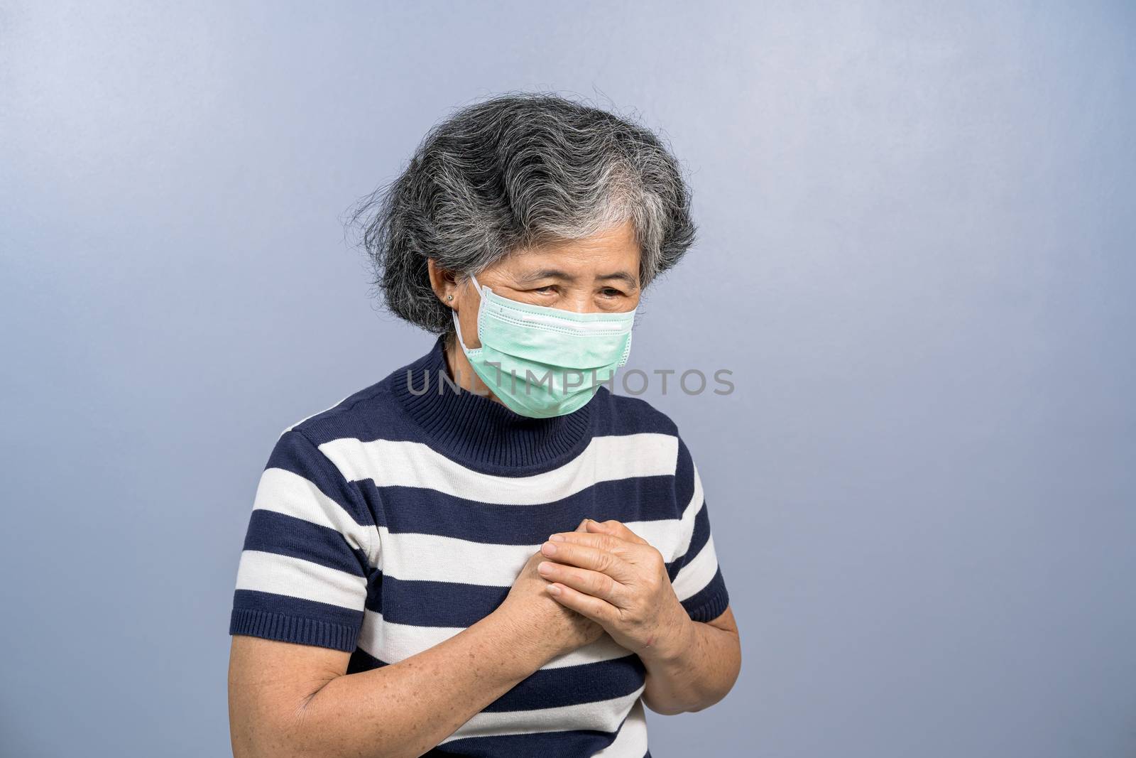 Asian Old woman wearing face surgical mask and  feeling pain ache touching chest having heart attack on blue color background, group risk of covid19 outbreak, protection against coronavirus concept