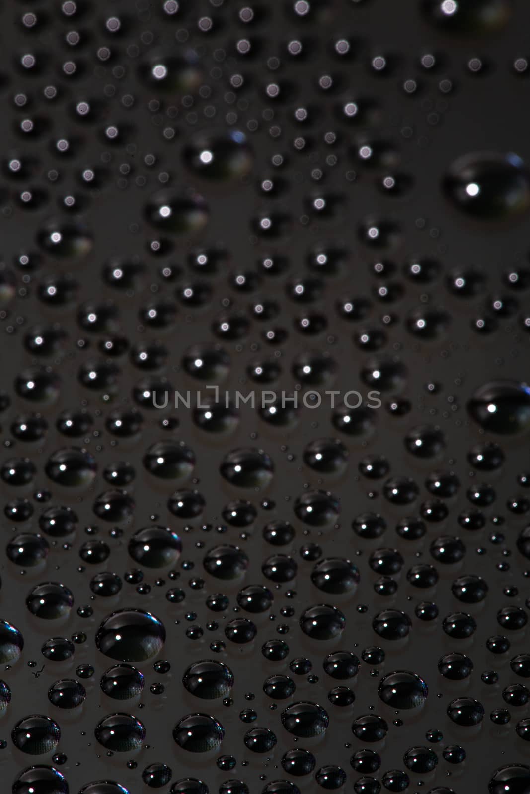 many small water drops on the black surface of cellphone hydriphobic coated glass screen, close-up with selective focus and visible subpixel rgb triads