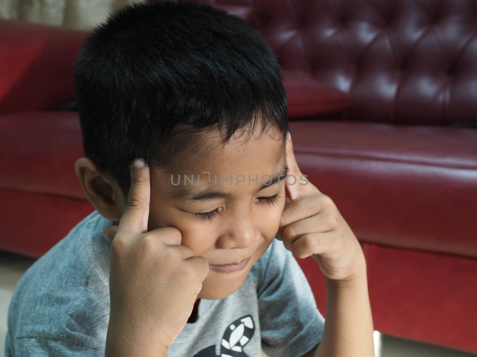 A boy in a headache On the background of the red sofa in the house.