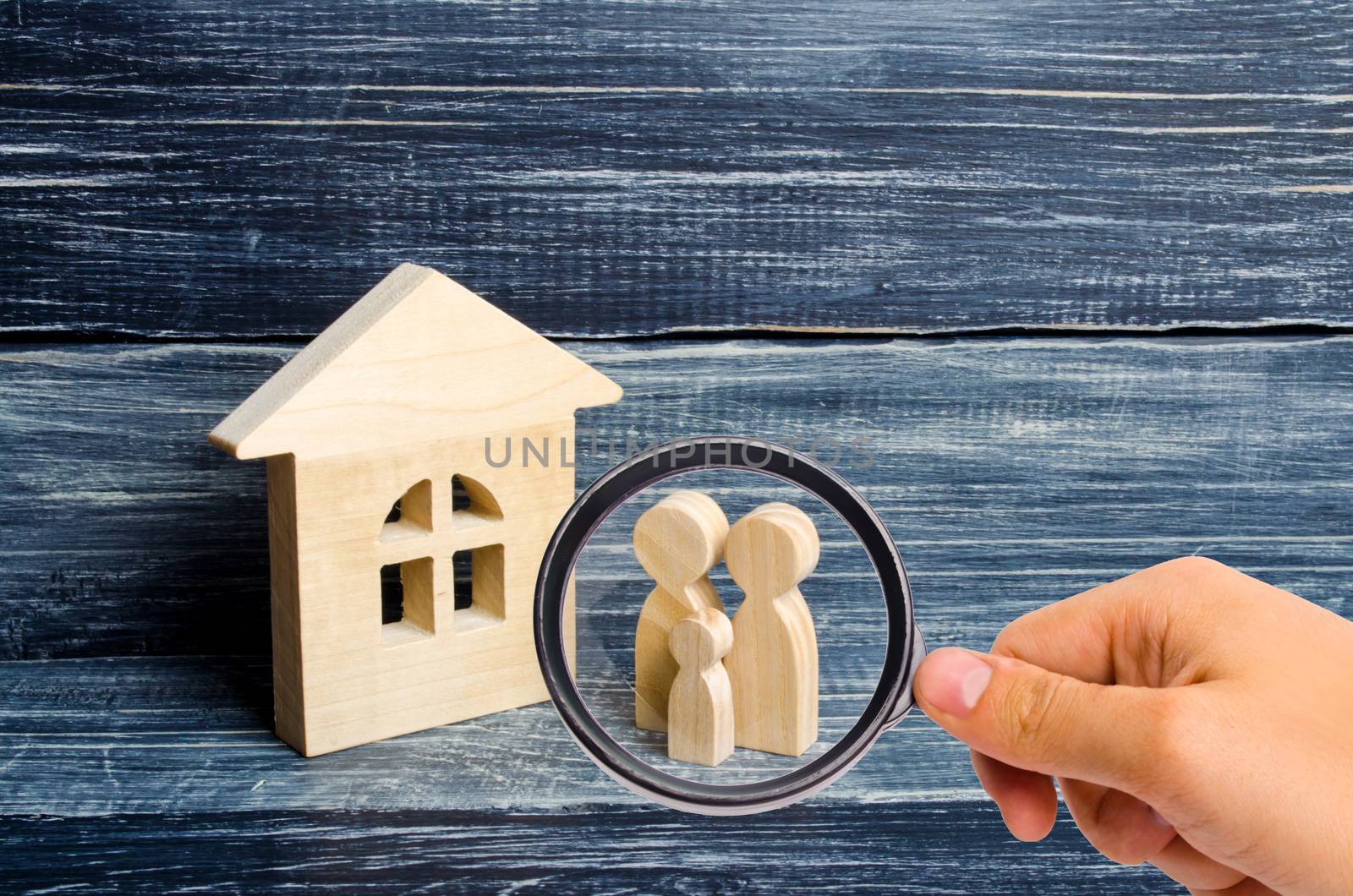 Magnifying glass is looking at the Family is standing near the house. Wooden figures of persons stand near a wooden house. The concept of a couple in love, cohabitants, parents, buyers