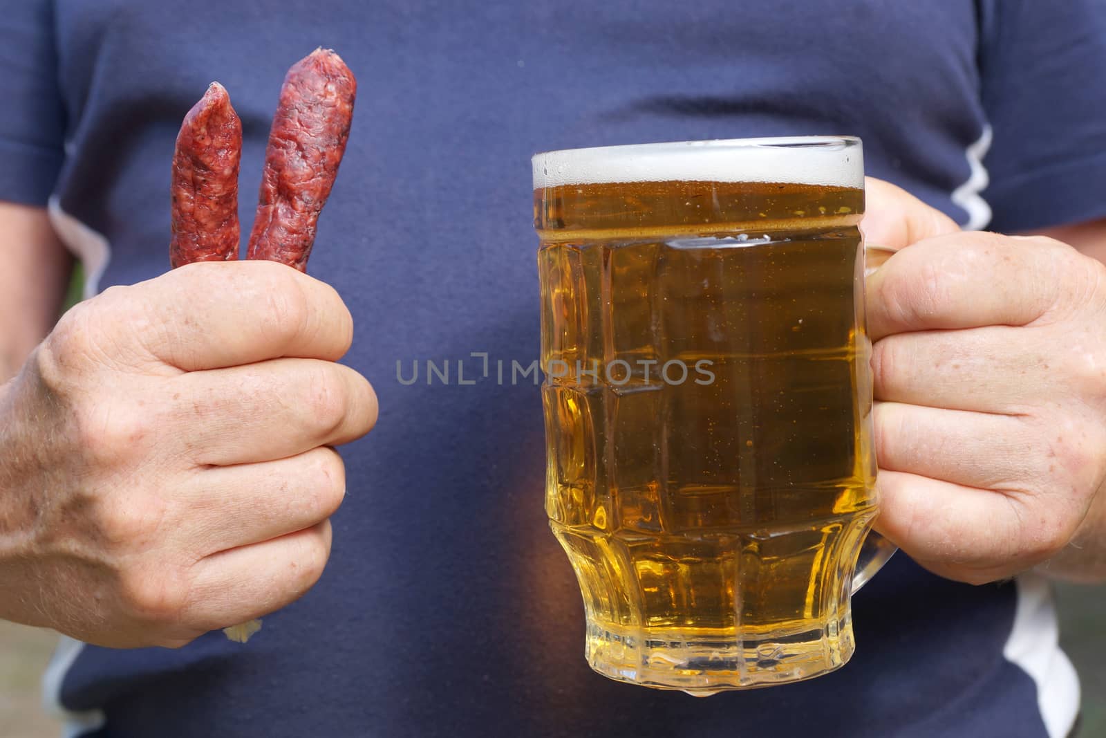 a mug with beer and sausages in the hands of a man close up