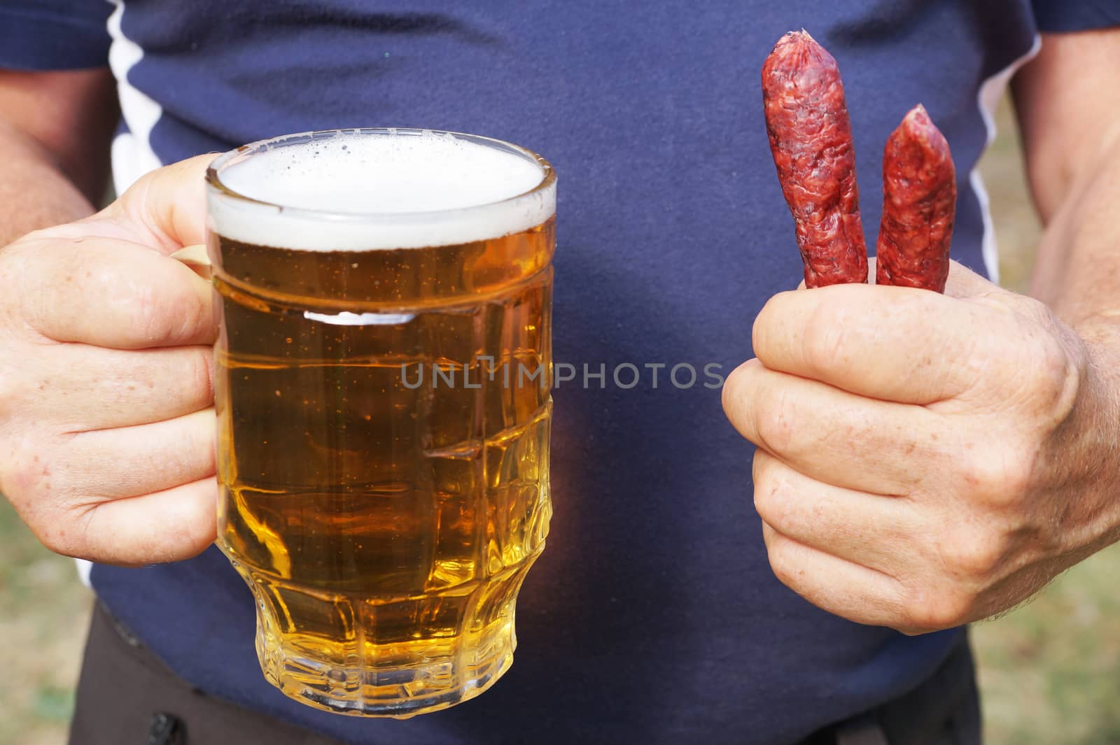 a mug with beer and sausages in the hands of a man close up