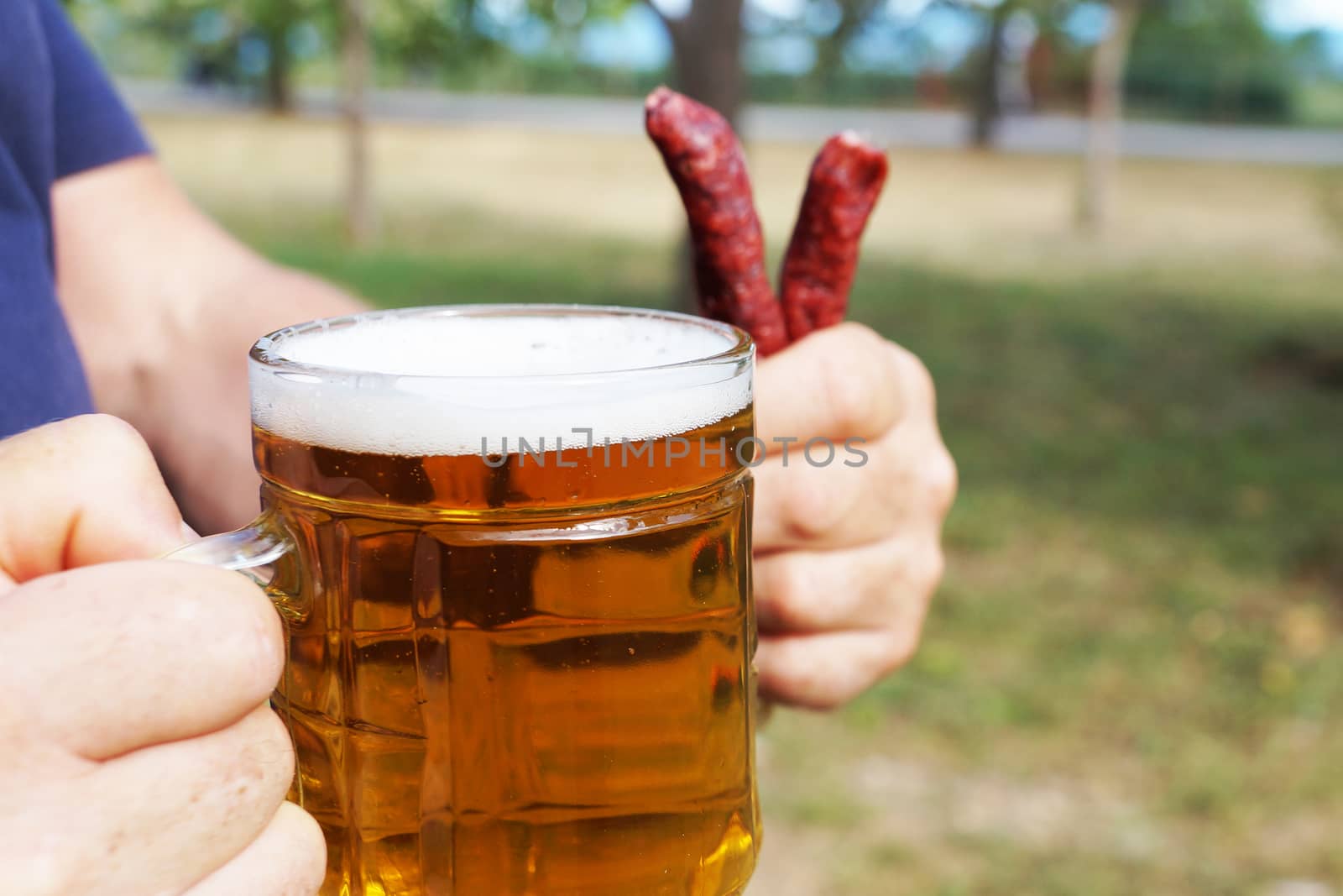 glass mug with beer and sausages in a man's hand on the background of nature close up