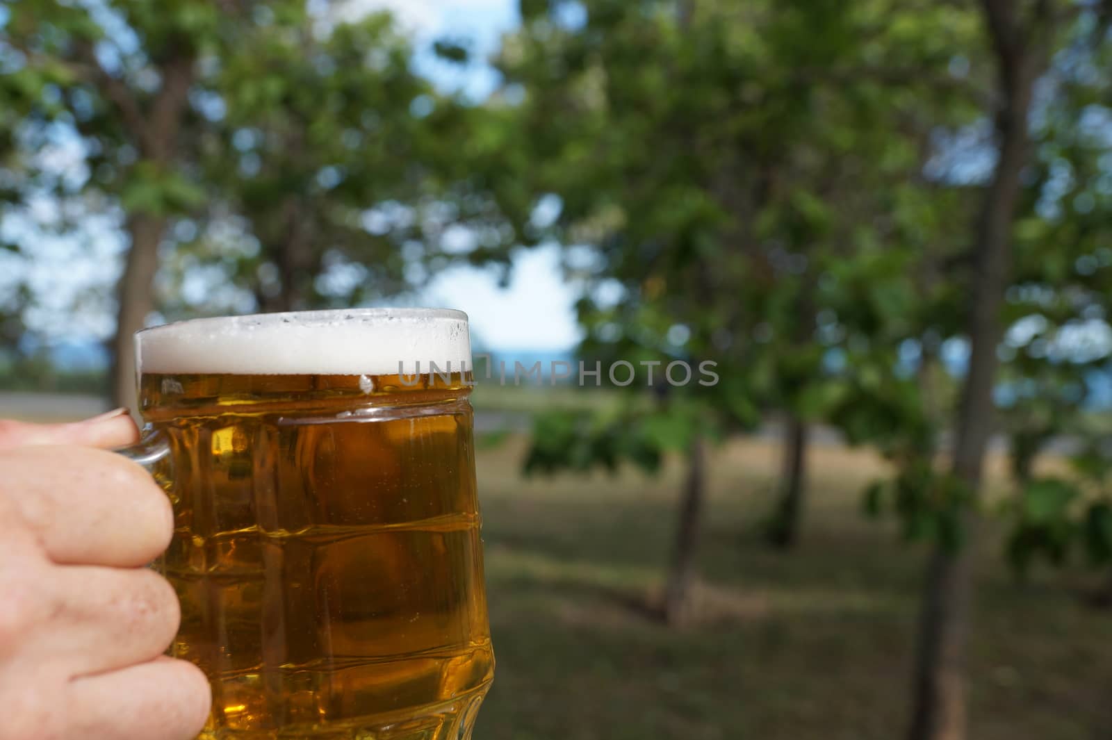 glass mug with beer and foam in a man's hand on the background of nature close up