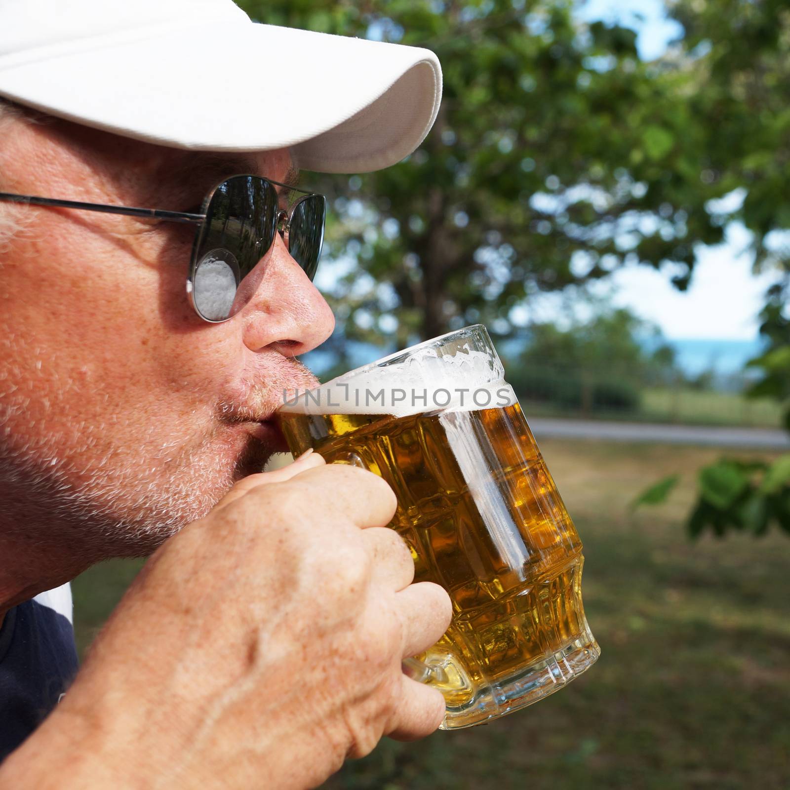 man drinks beer from a large glass mug in nature by Annado