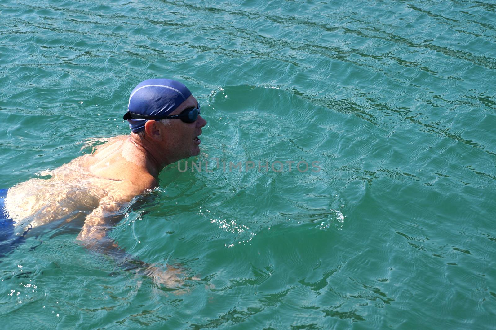 man in swimming goggles swims in the sea . by Annado