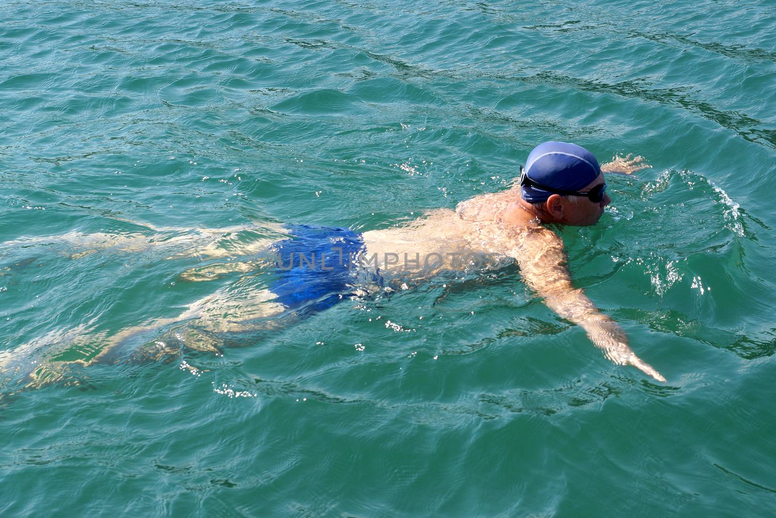 man in swimming goggles swims in the sea . by Annado