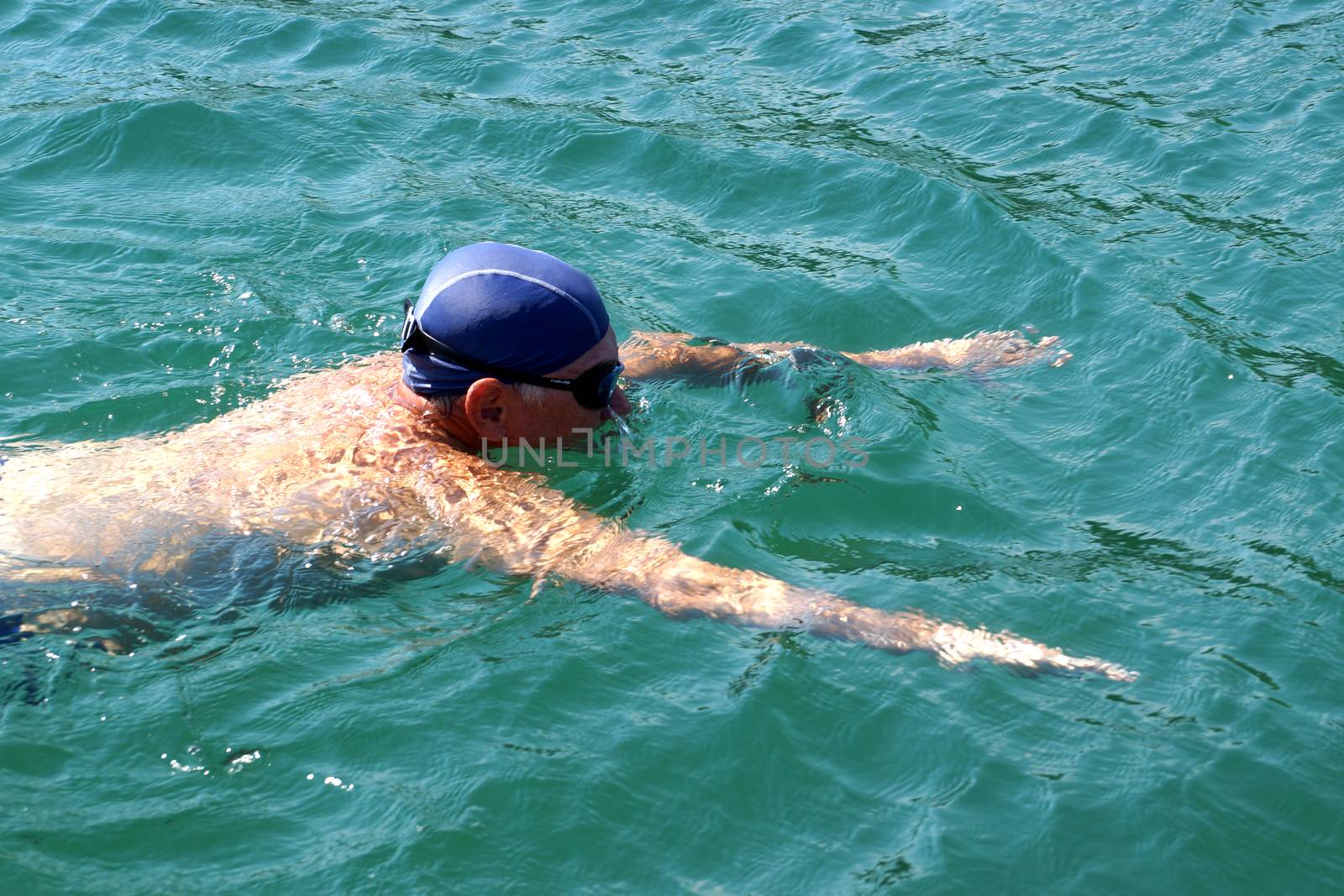 man in swimming goggles swims in the sea . by Annado